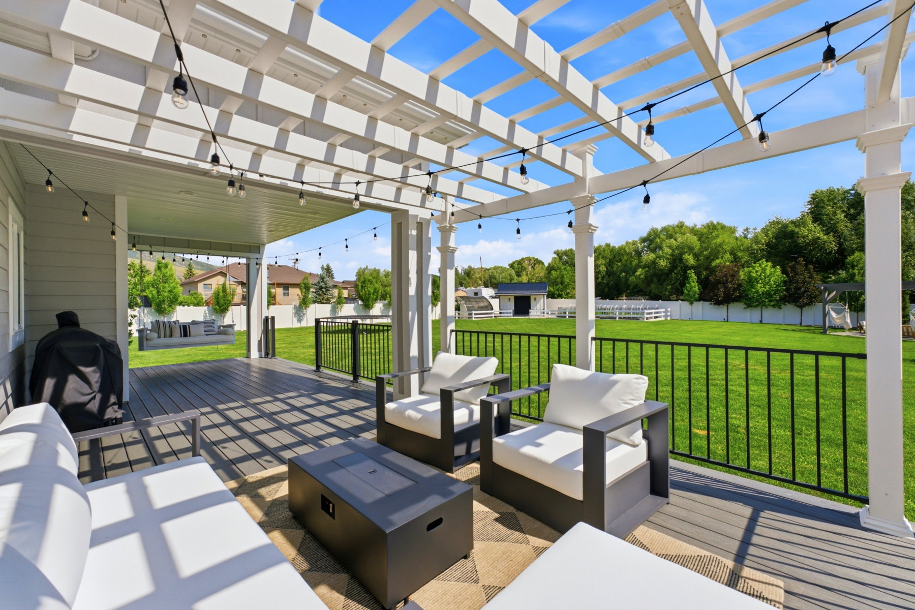 Expansive outdoor living area featuring a covered patio, composite decking, and a white pergola with string lighting