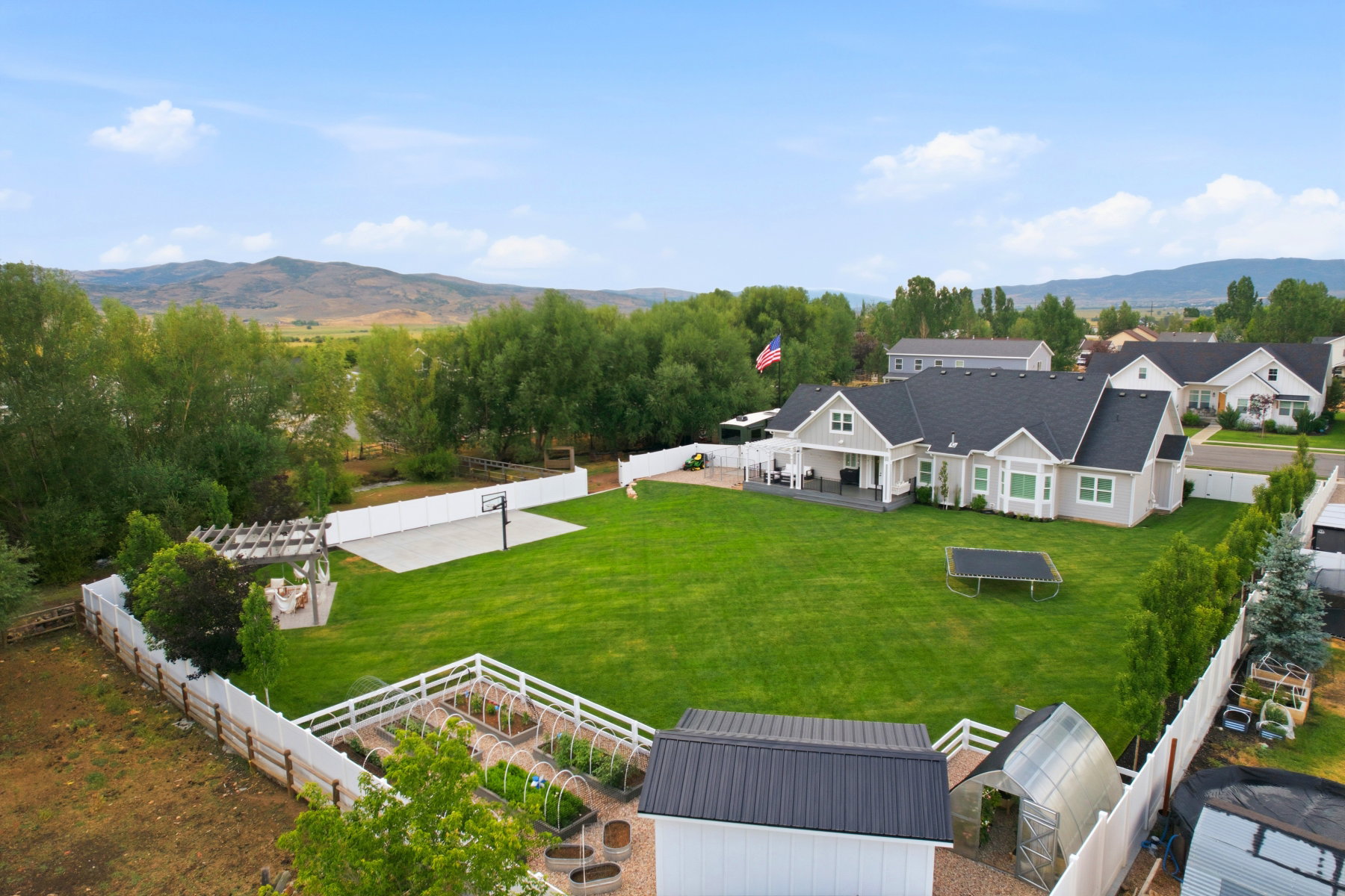 Expansive backyard featuring a manicured lawn, a half-court sports area, and a pergola-covered patio