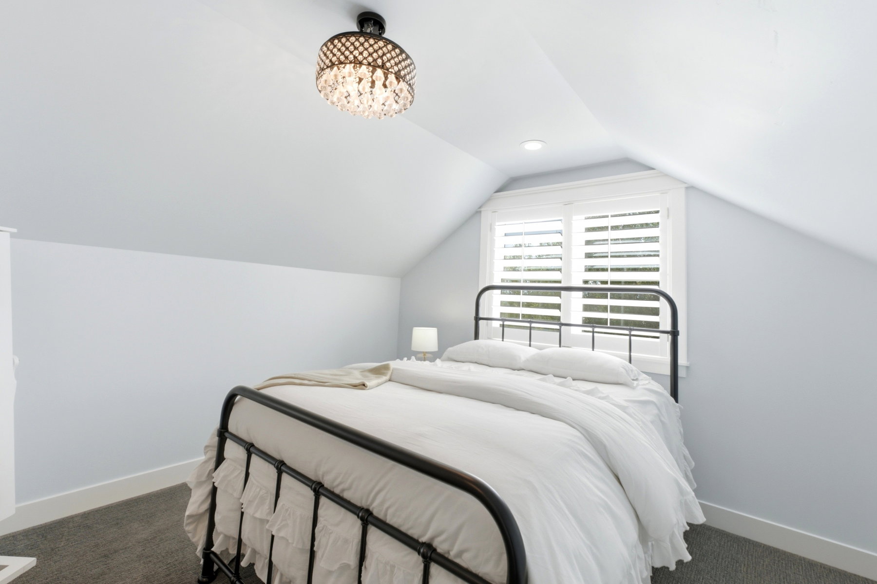 Attic bedroom featuring an angled ceiling, a crystal chandelier, recessed lighting, a window with plantation shutters, and dark gray carpeting