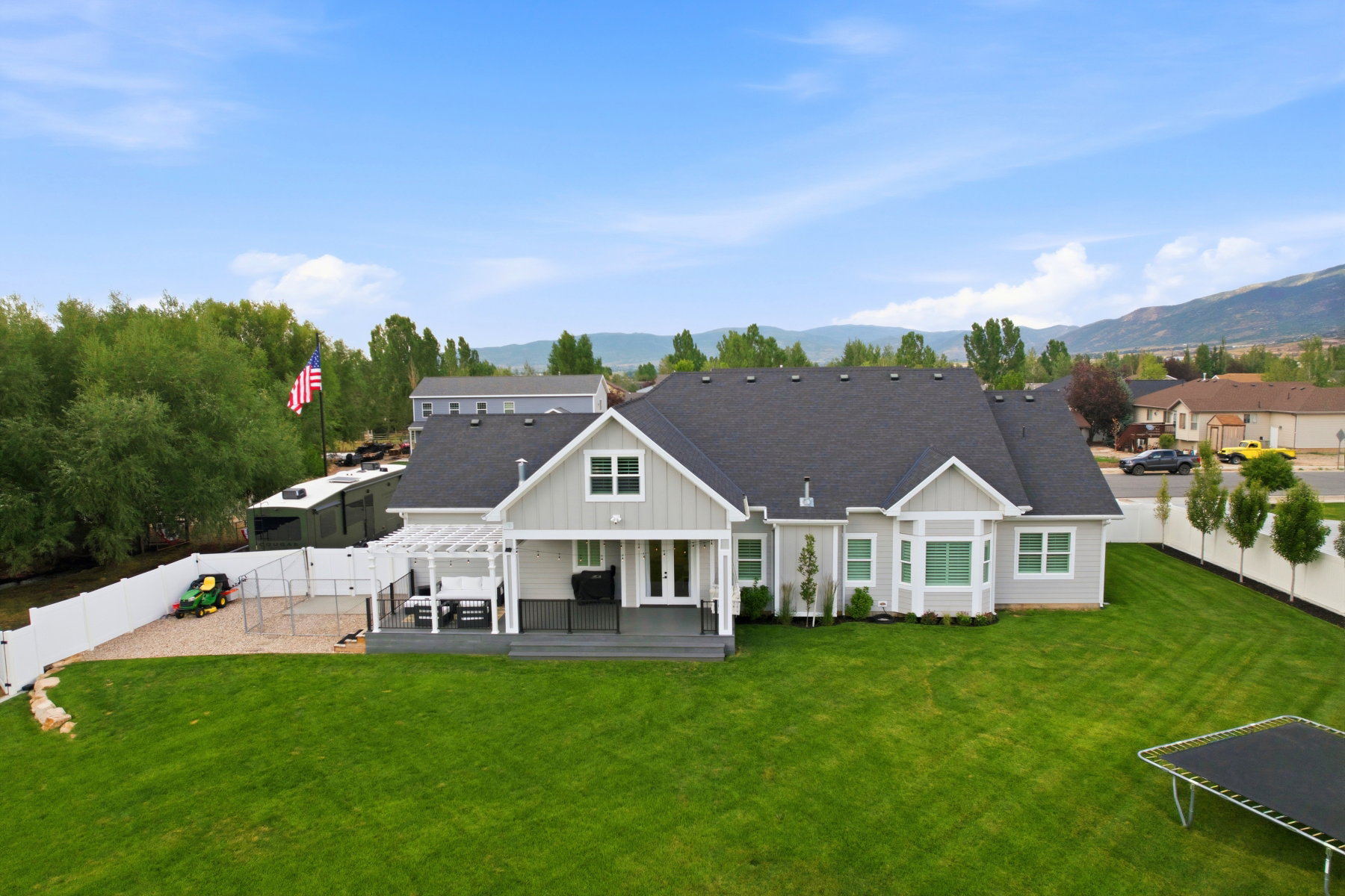 Spacious backyard featuring a large green lawn, an extensive dark-toned deck with a white pergola, and a white vinyl privacy fence