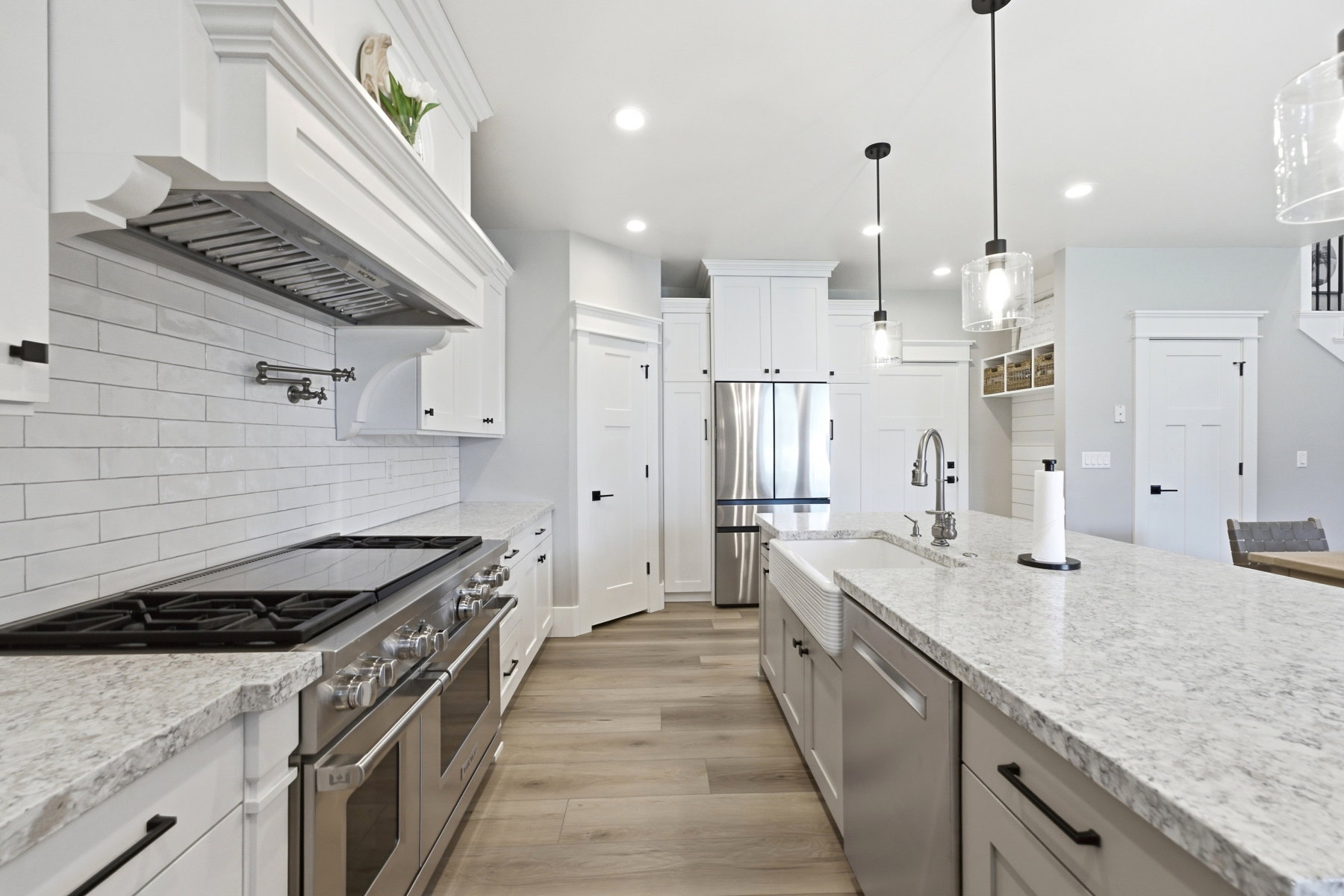 Gourmet kitchen featuring a professional-grade range, full subway tile backsplash, white shaker cabinetry, and a large central island with a farmhouse sink