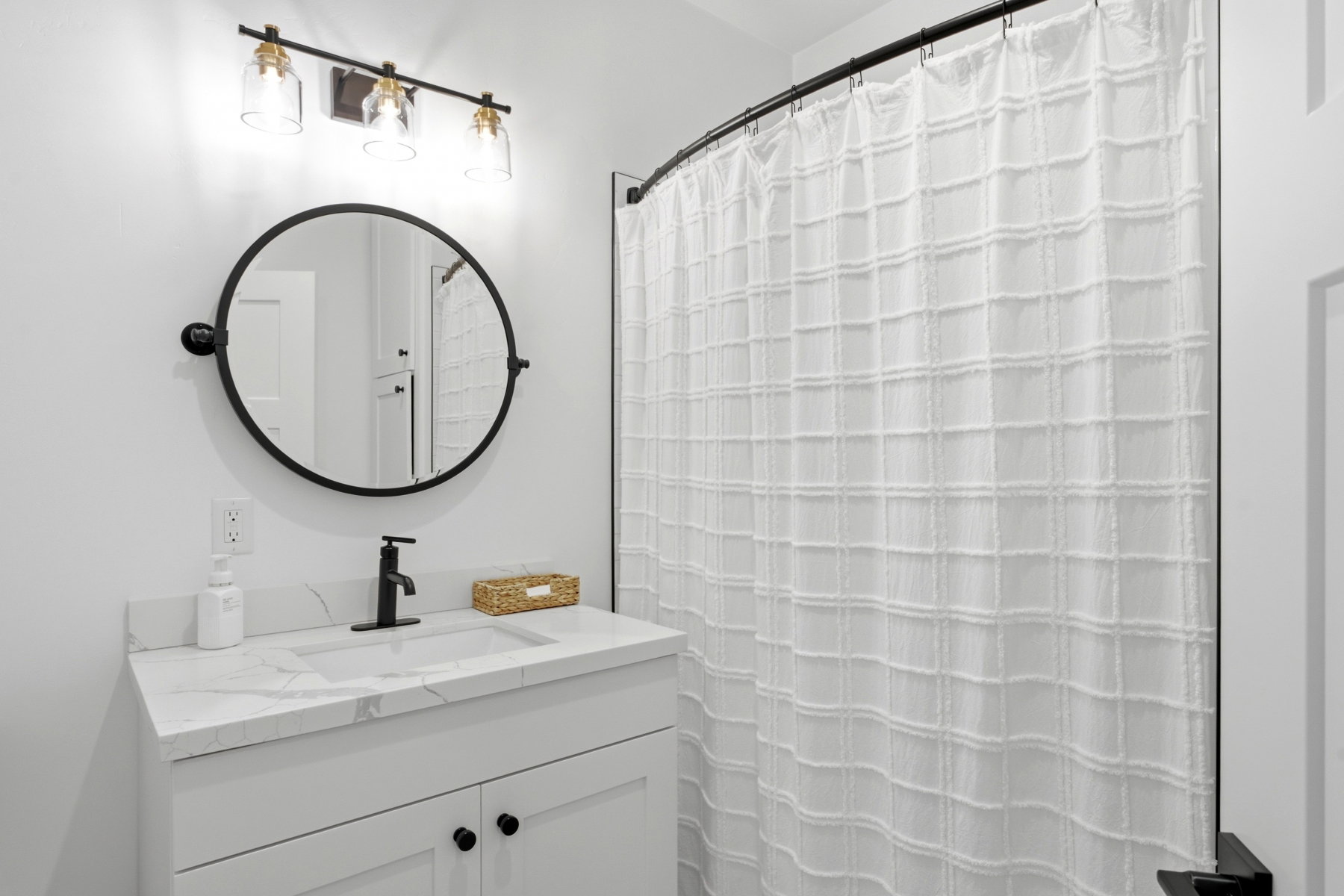 Bathroom featuring a white vanity with a white countertop and integrated sink, a black single-handle faucet, and a round black-framed mirror