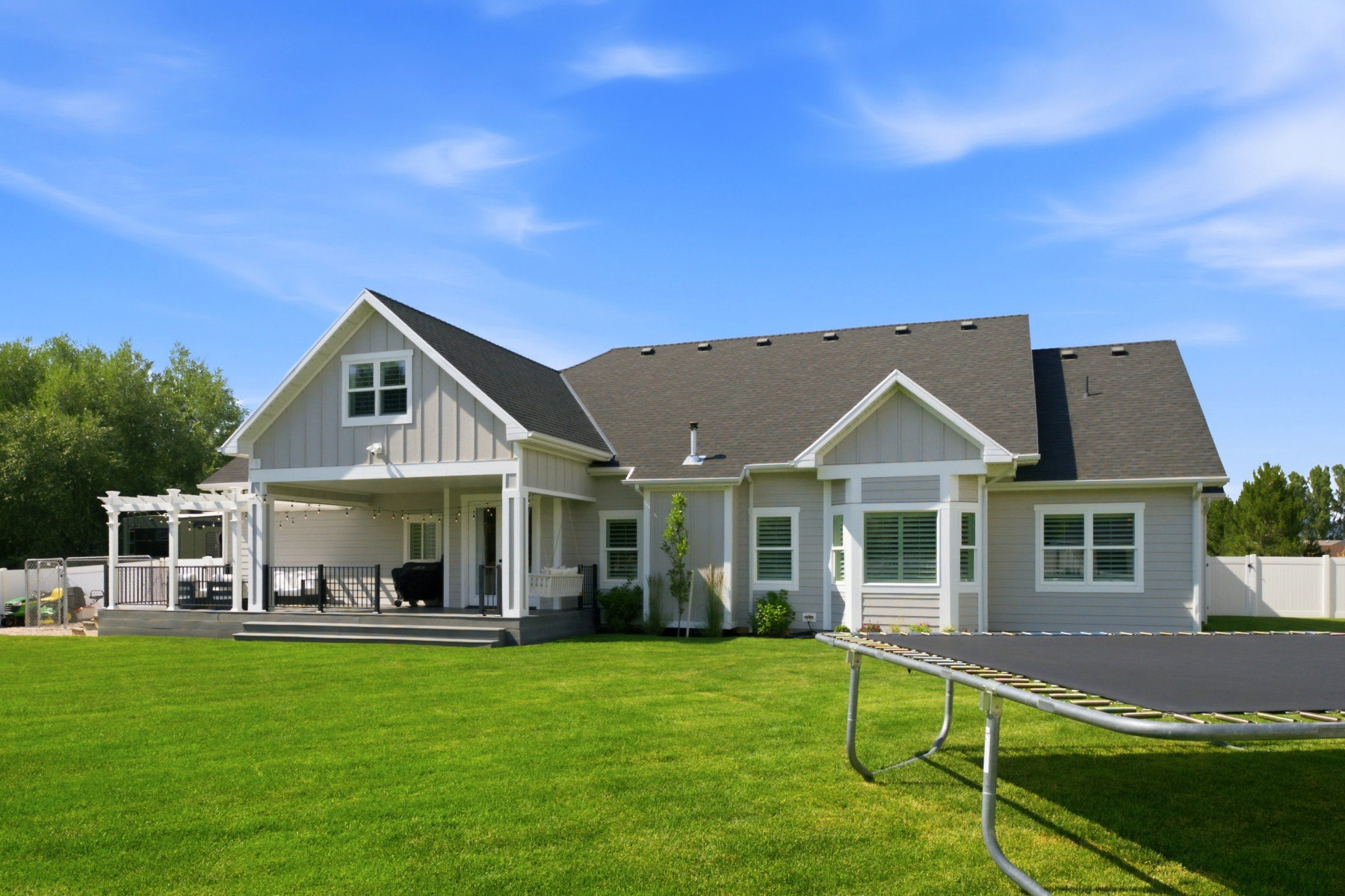 Spacious backyard featuring a manicured lawn, an expansive covered patio, and a tiered deck with a white pergola