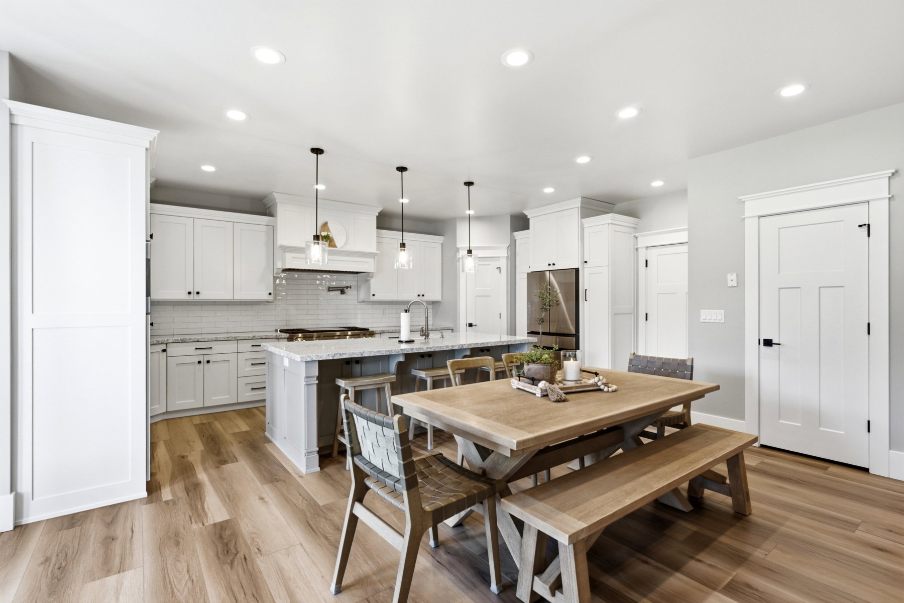 Spacious kitchen featuring white shaker-style cabinetry, a large island with seating, stainless steel appliances, a subway tile backsplash, and wood-finish flooring