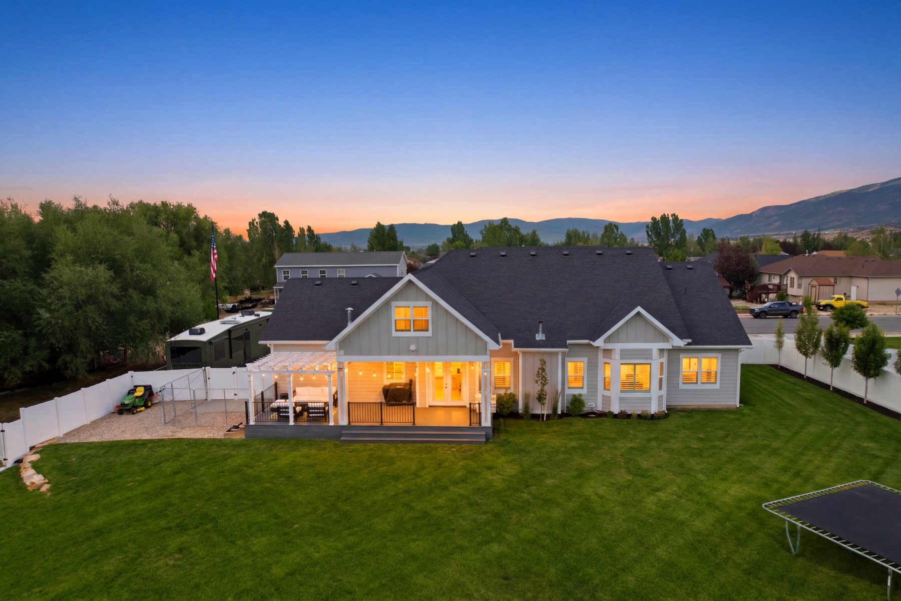 Expansive backyard featuring a manicured lawn, a large deck with a pergola, and a white vinyl fence