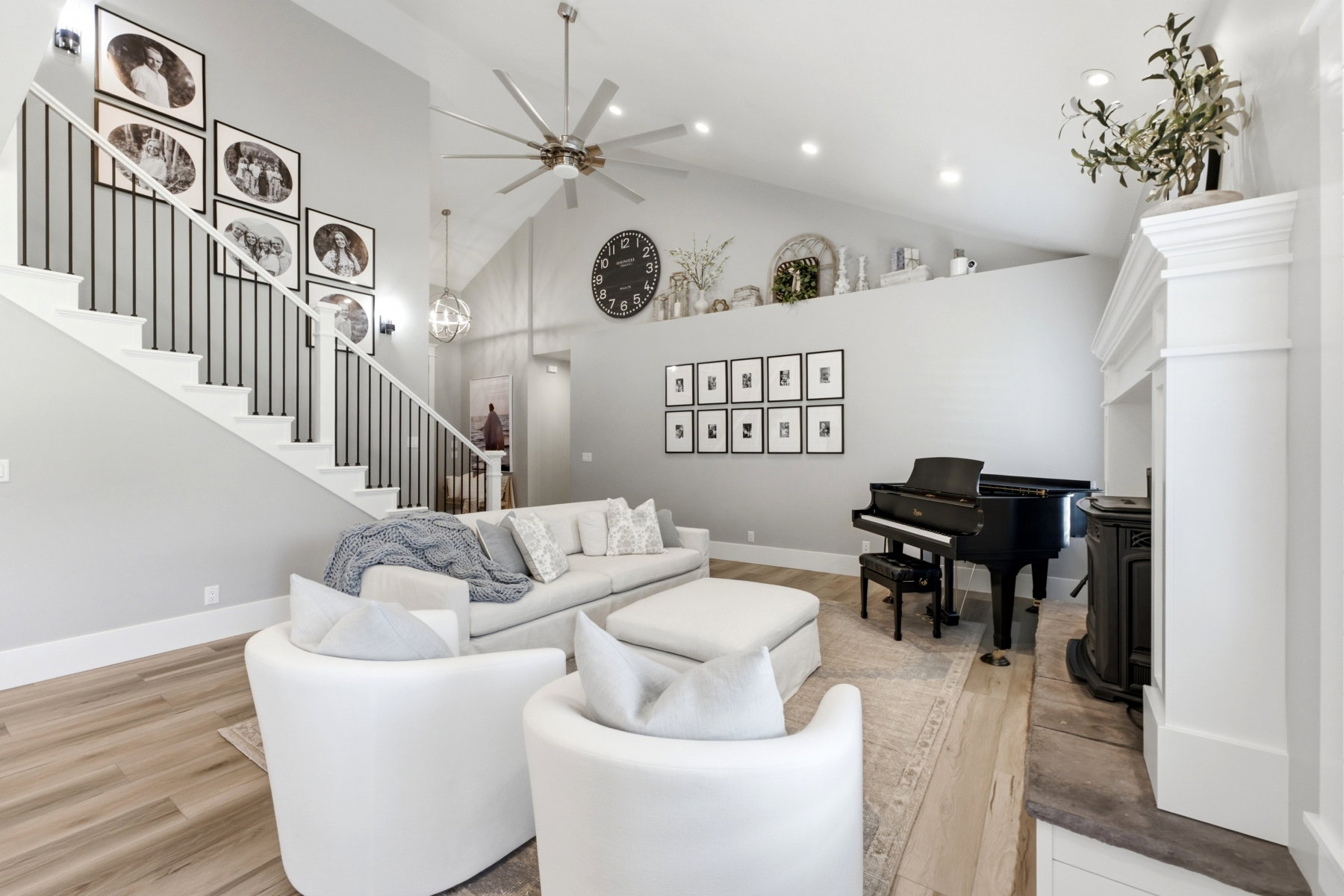 Spacious living area featuring high vaulted ceilings, wood-finish flooring, a grand staircase with black metal railings, a white fireplace with a dark hearth, and recessed lighting