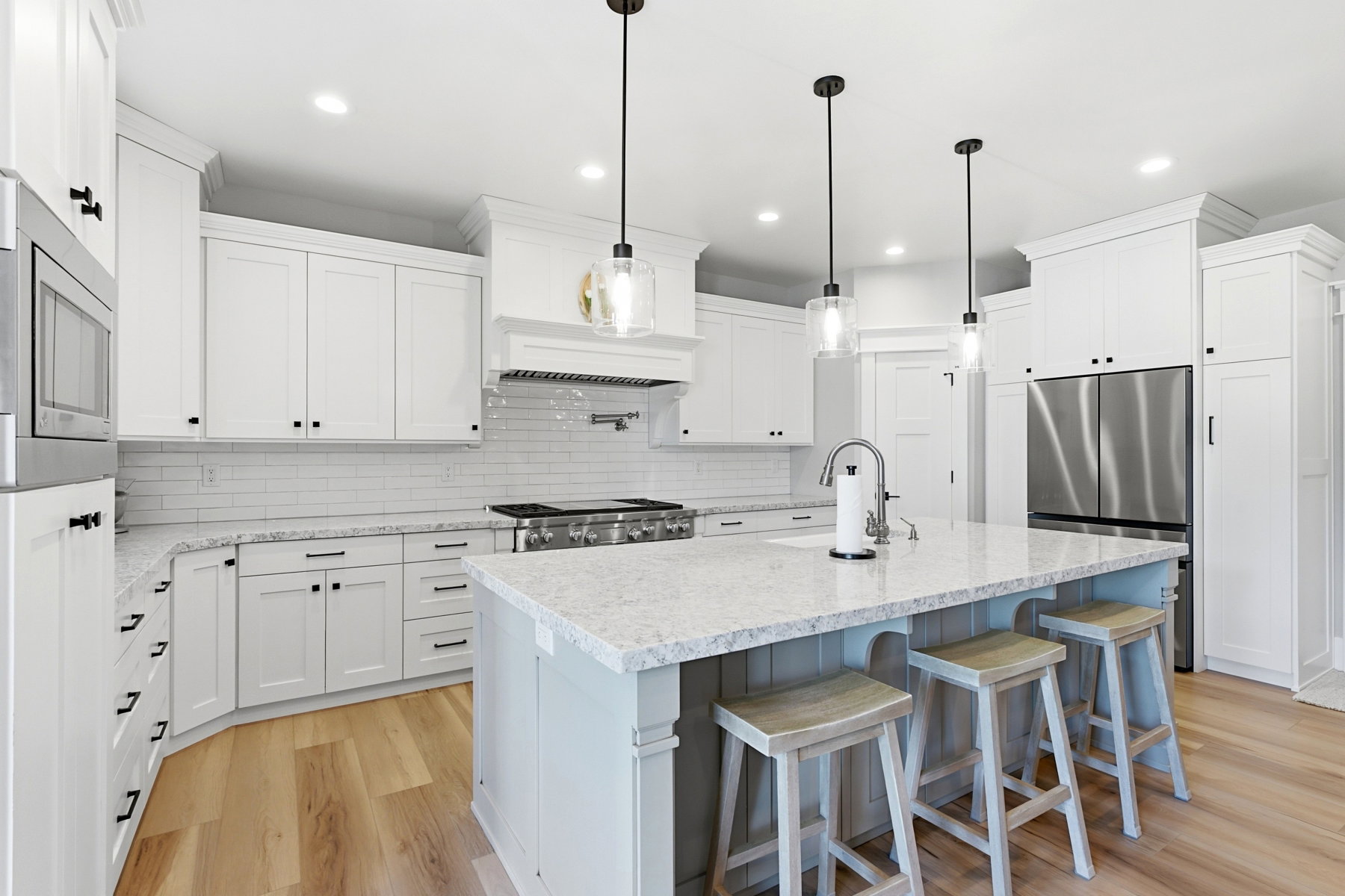 Modern kitchen featuring light wood-finish flooring, white shaker-style cabinetry, and a subway tile backsplash