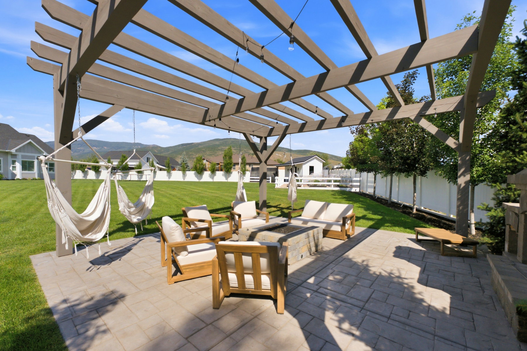 Expansive backyard featuring a stone patio, a large pergola, and a built-in fire pit