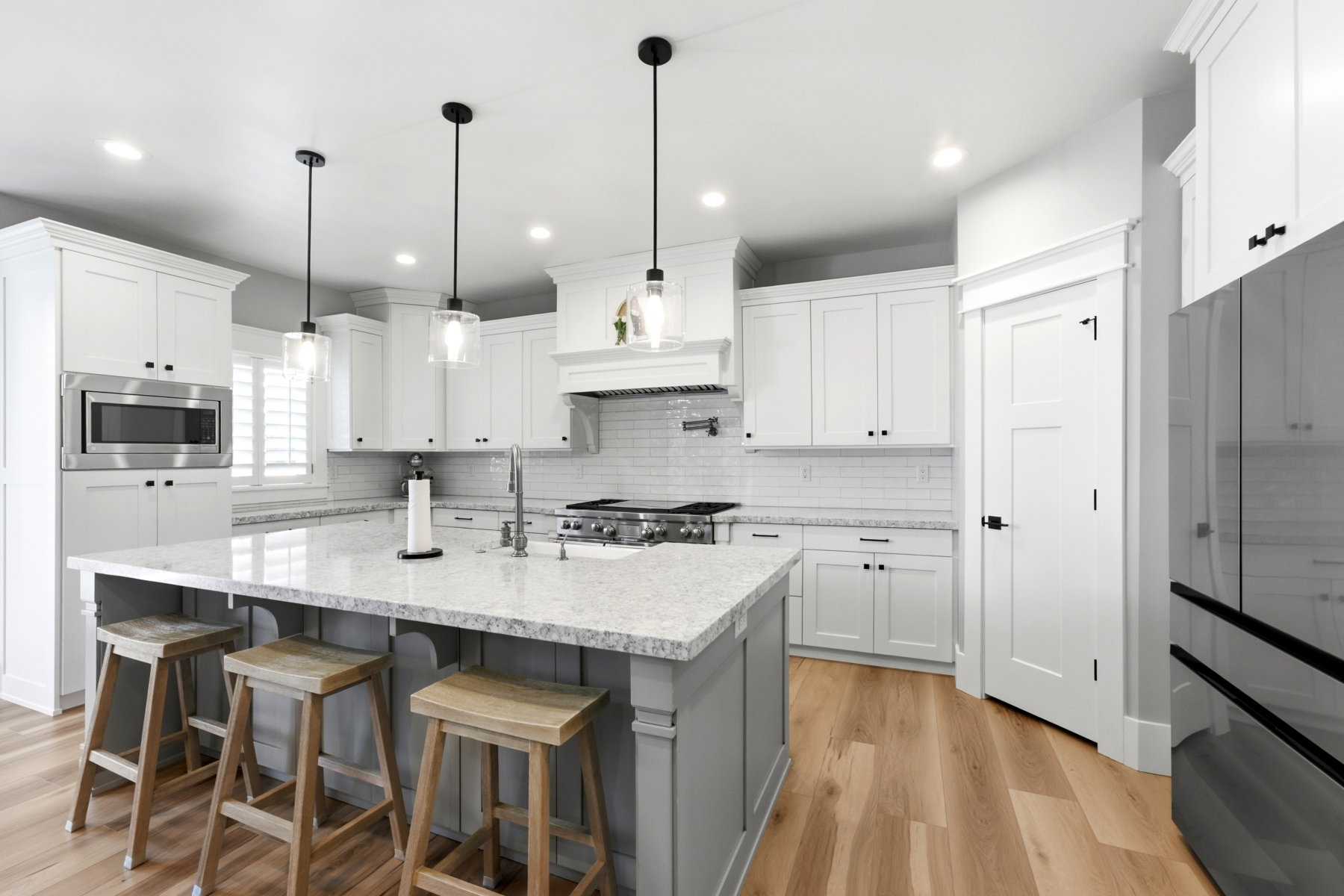 Modern kitchen with a large island featuring a speckled countertop, contemporary pendant lighting, recessed ceiling lights, white shaker-style cabinetry, and wood-finish flooring