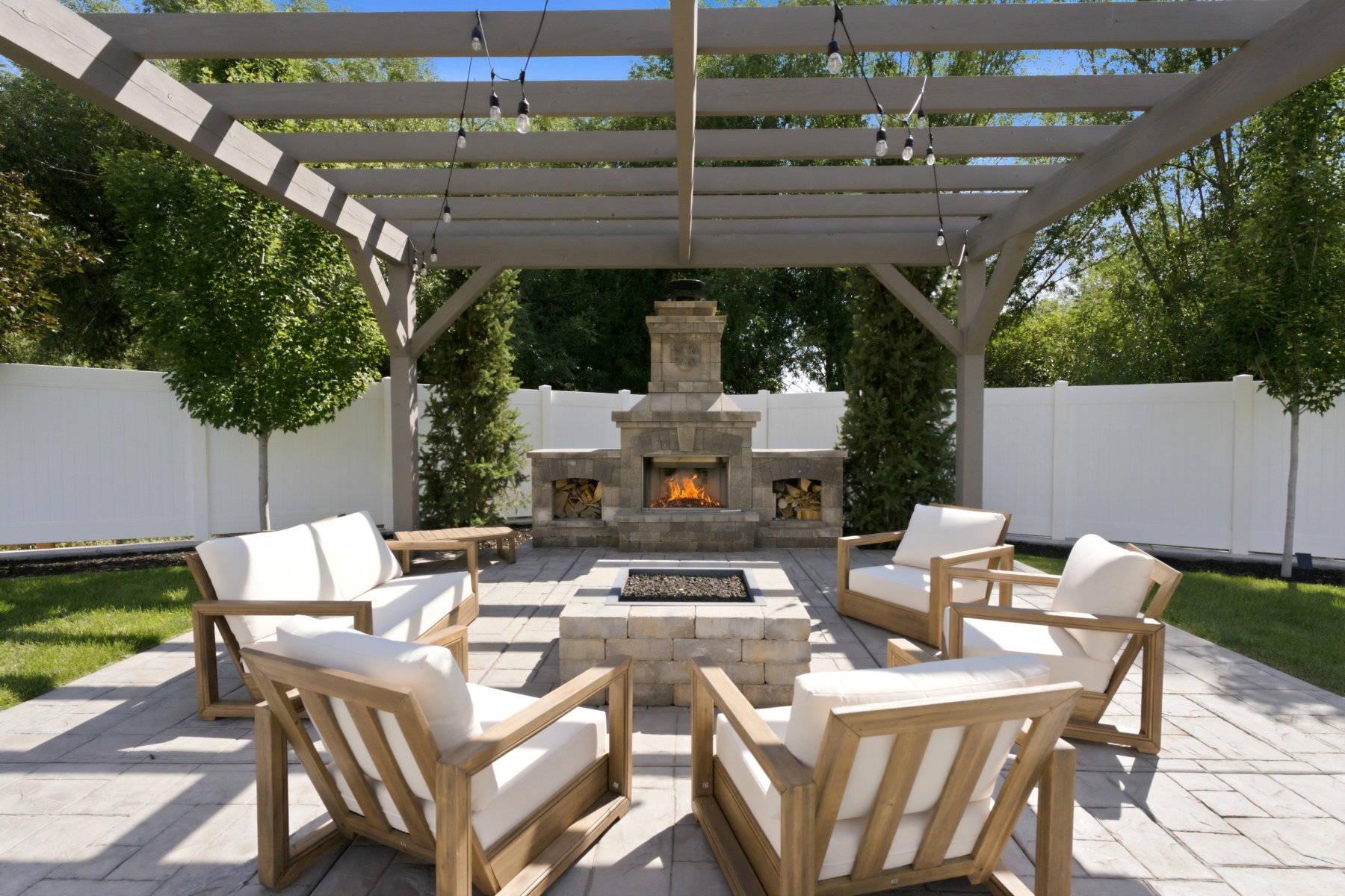 Expansive patio featuring a stone fireplace, integrated fire pit, and a pergola with string lighting