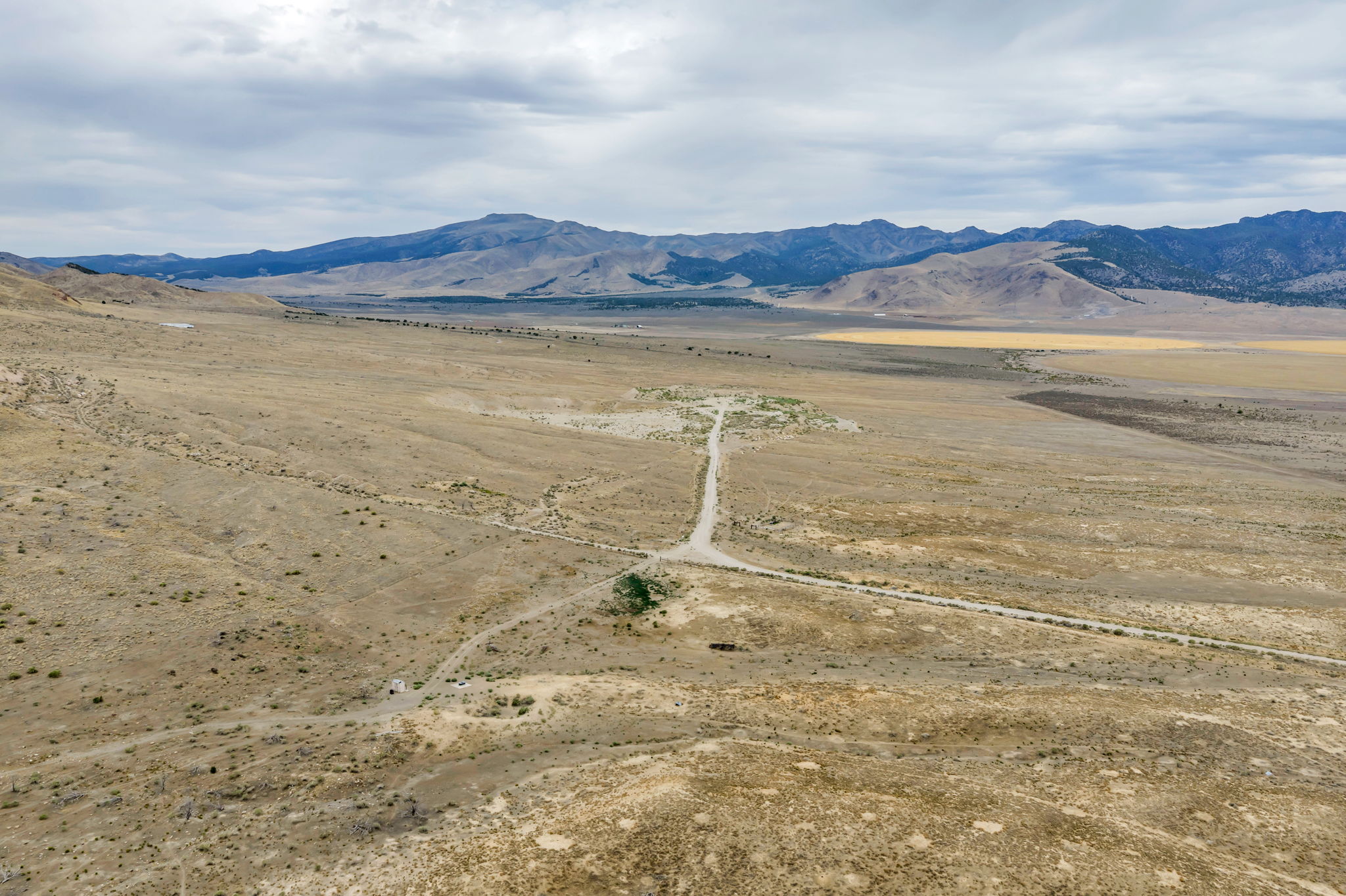Expansive open land featuring a meandering dirt road, distant mountain range, varied terrain, and broad skies