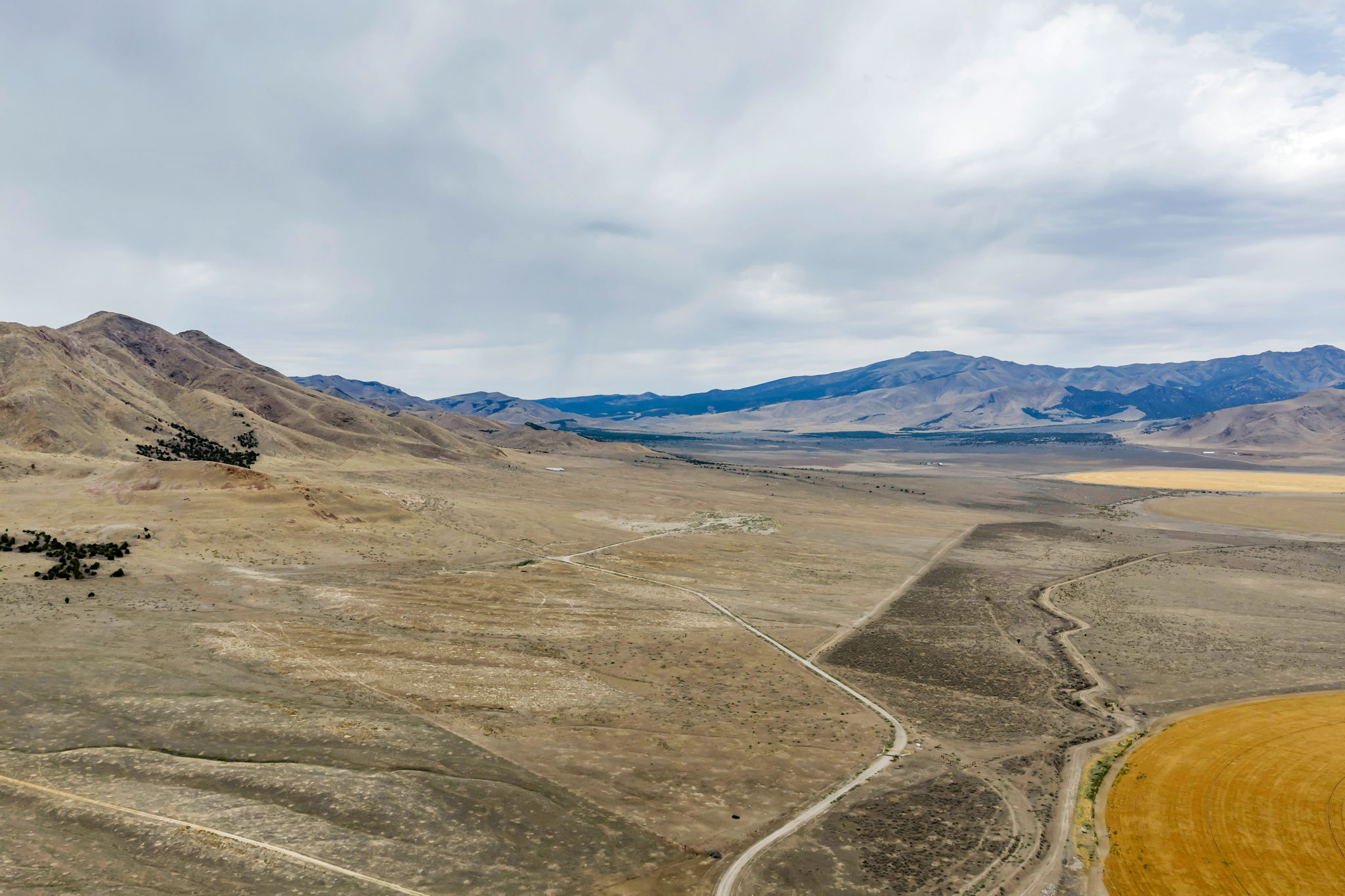 Expansive open terrain featuring distant mountains, a dirt road, and a circular agricultural field