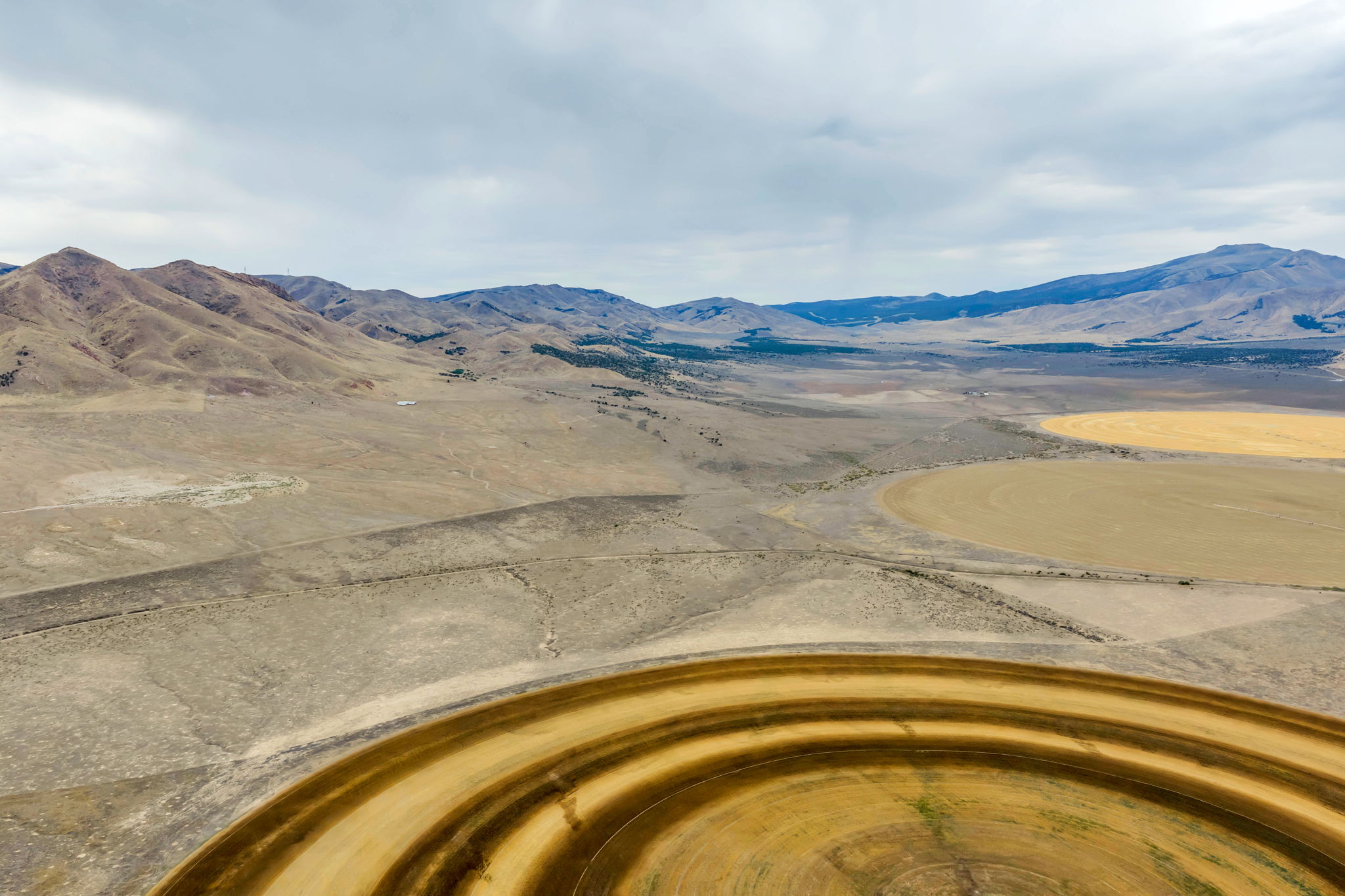 Expansive rural landscape featuring a prominent circular field, additional cultivated land, and distant mountain ranges