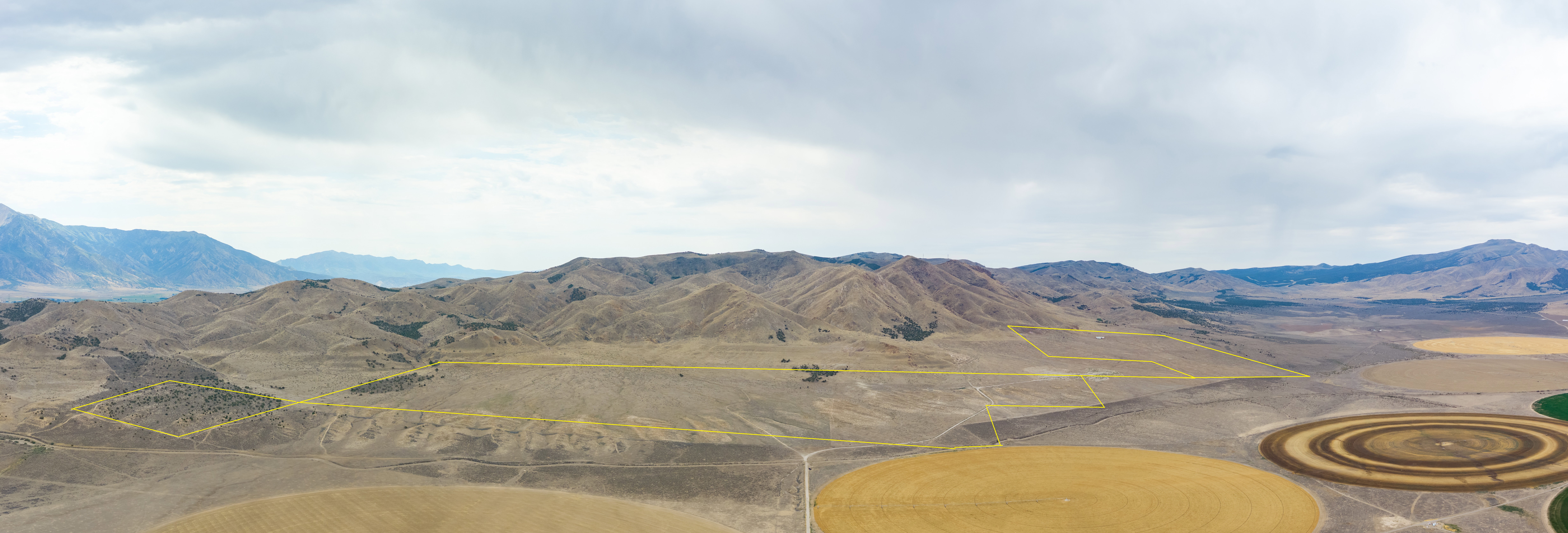 Expansive undeveloped land featuring natural terrain and distant mountains under a cloudy sky