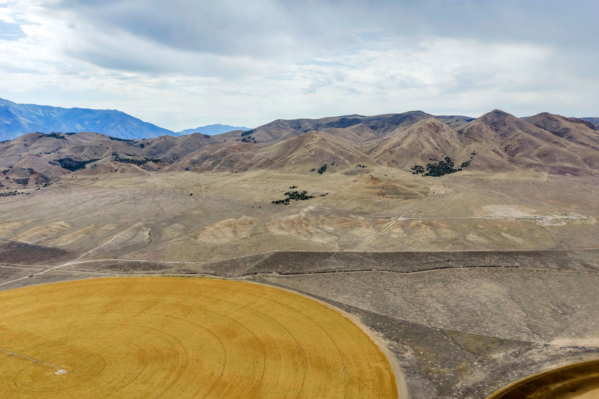 Expansive land featuring a circular cultivated field, surrounded by vast open terrain and distant mountain ranges