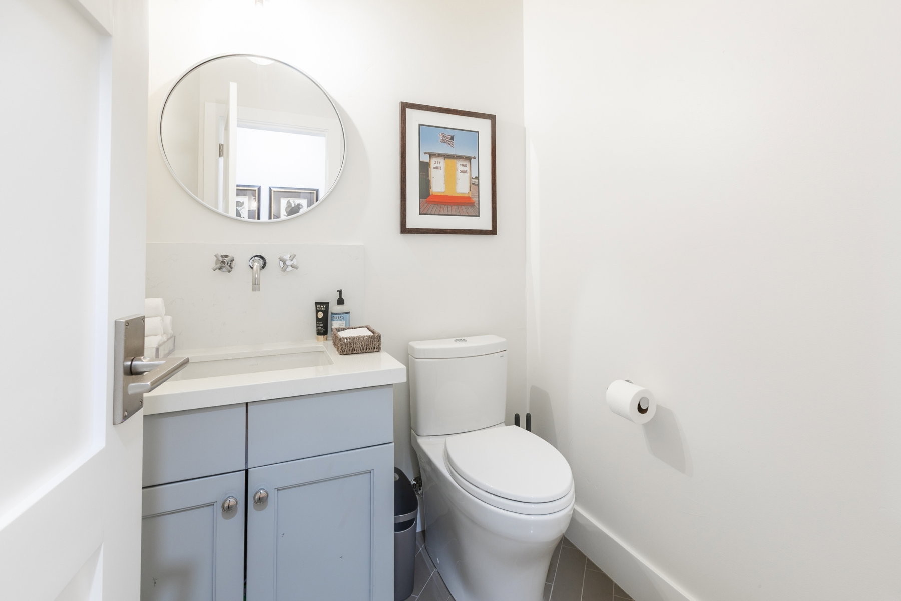 Compact bathroom featuring a white toilet, light gray vanity with a single basin, and a circular mirror