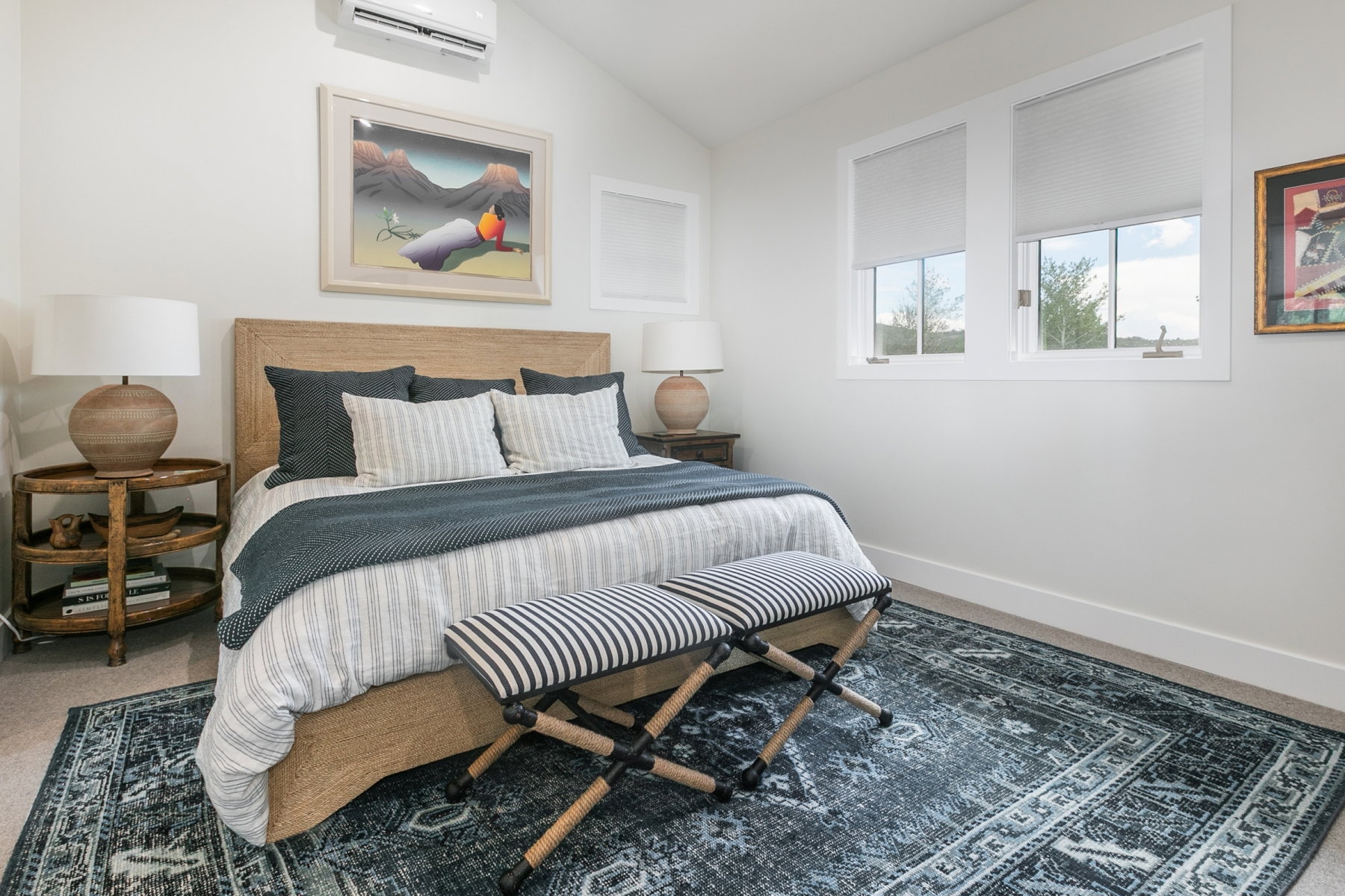 Bedroom featuring a wood-finish bed frame, white walls, two windows with blinds, a patterned area rug, and an installed air conditioning unit