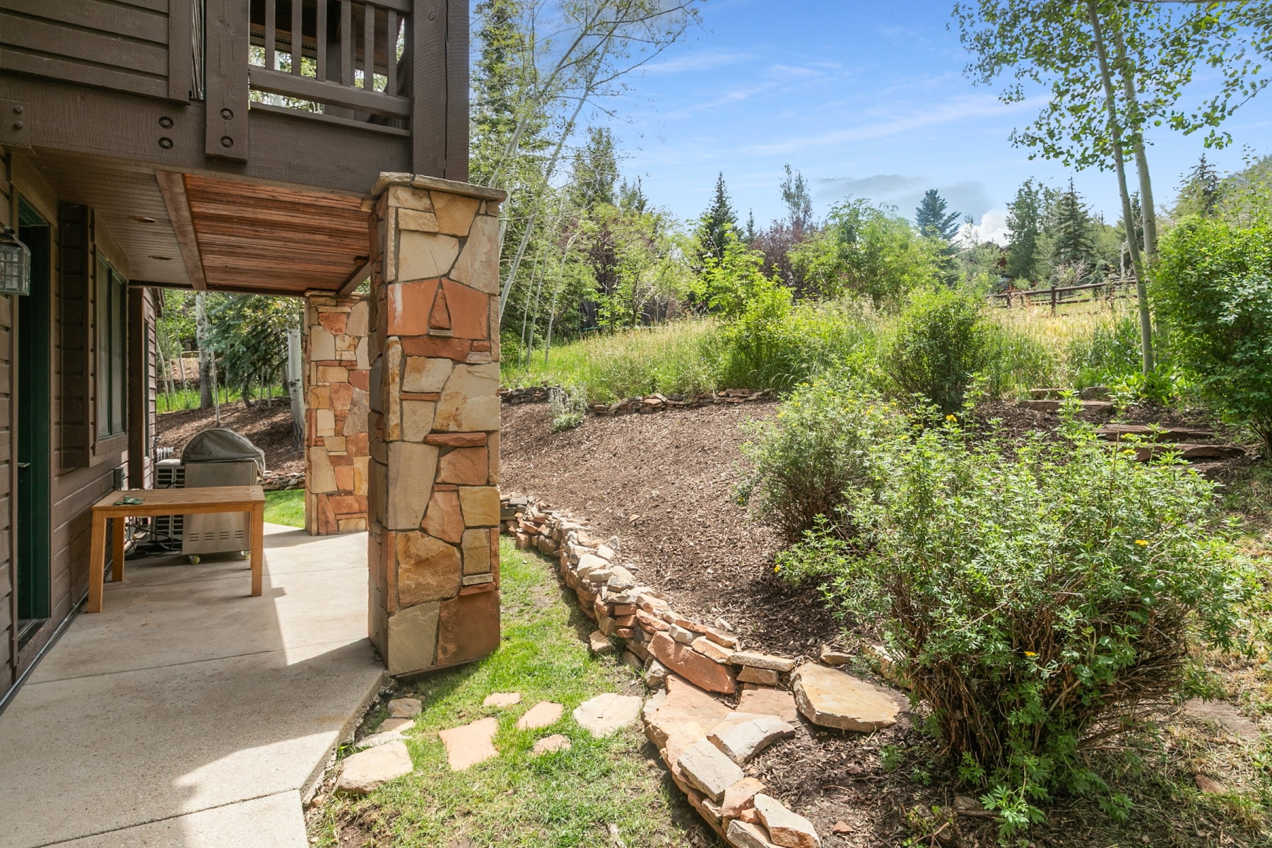 Covered outdoor patio with concrete flooring, supported by stone veneer columns and featuring a wood-plank ceiling