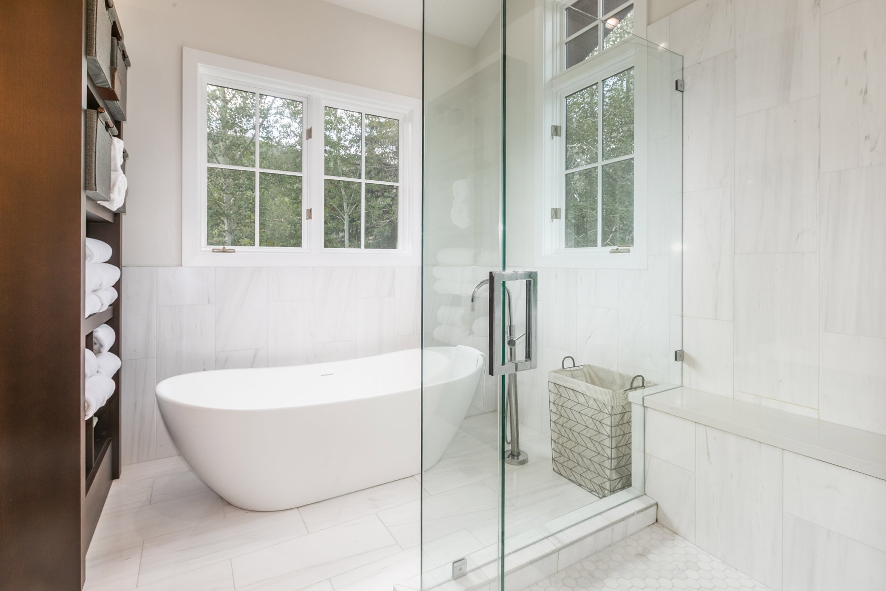 Freestanding soaking tub with floor-mounted faucet, surrounded by large format tile flooring and wainscoting