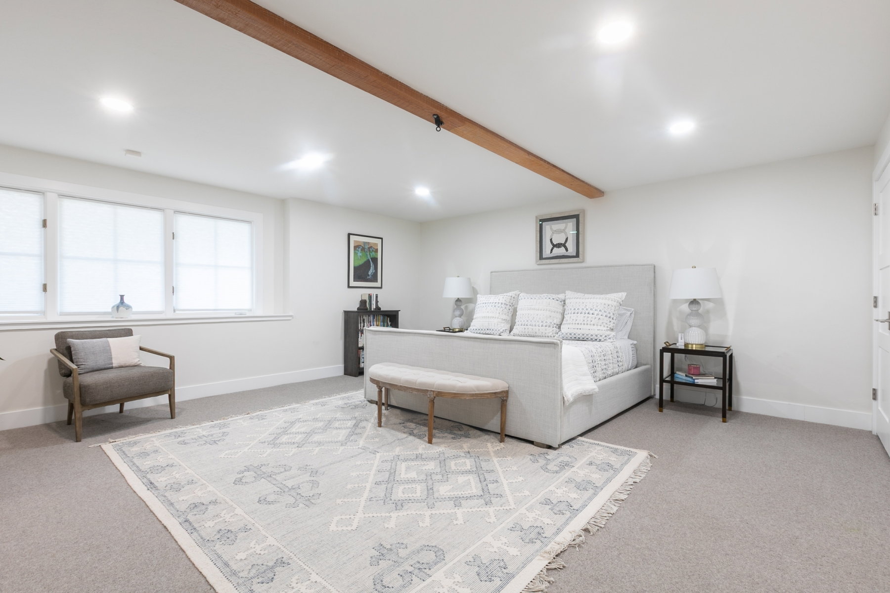 Spacious room featuring neutral carpeting, white walls, and a prominent wood ceiling beam