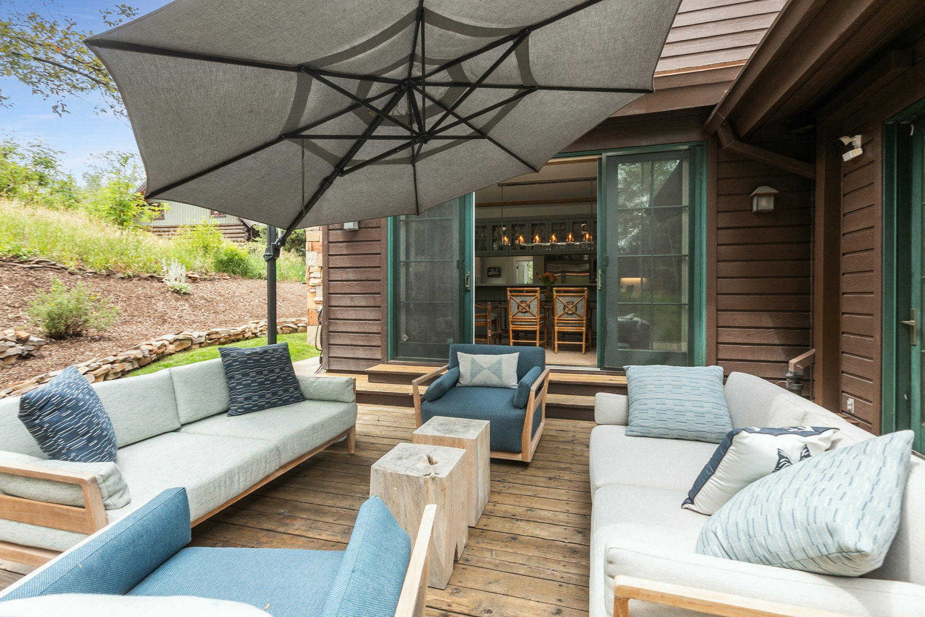 Expansive wood-finish deck with a large offset patio umbrella, multiple seating areas, and direct access to an interior space through double glass-paneled doors