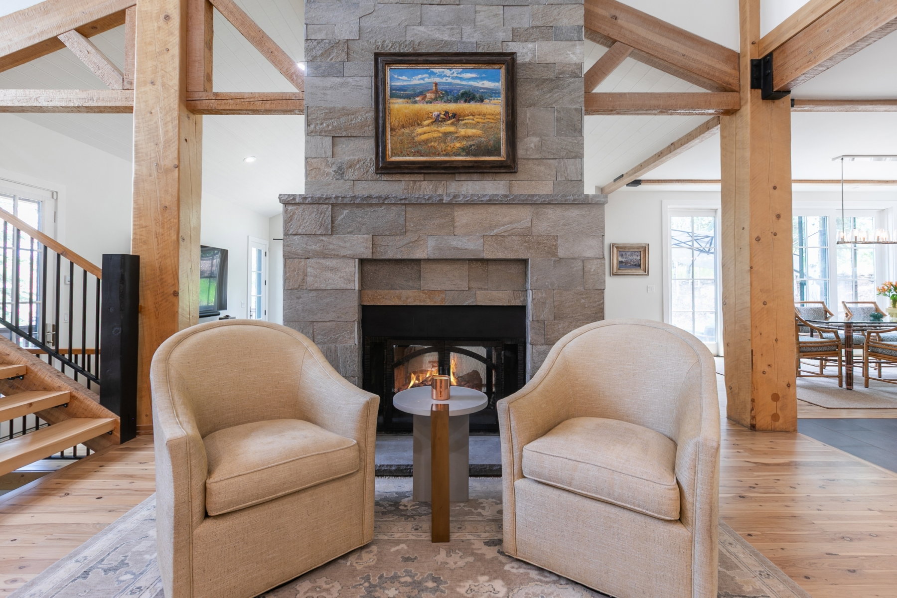 Stone-clad fireplace with hearth, exposed timber beams, wood-finish flooring, and open staircase with metal balusters