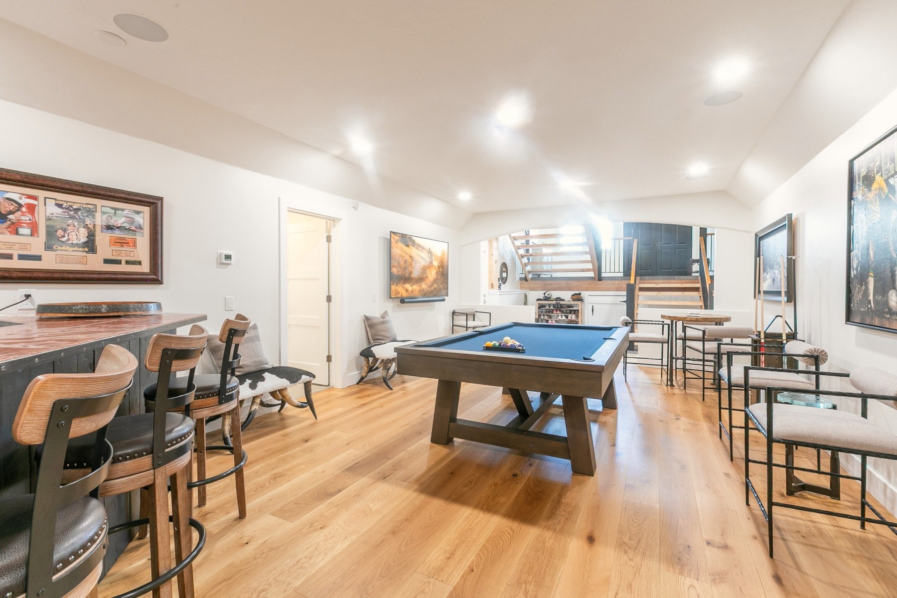 Expansive recreation room featuring light wood-finish flooring, recessed lighting, a built-in bar, and a visible staircase with wood treads and black risers