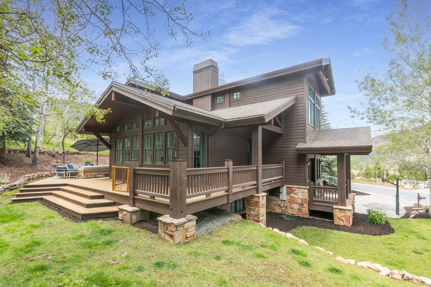 Brown siding exterior with a multi-level wood deck, stone accents, extensive windows, and a covered porch entry
