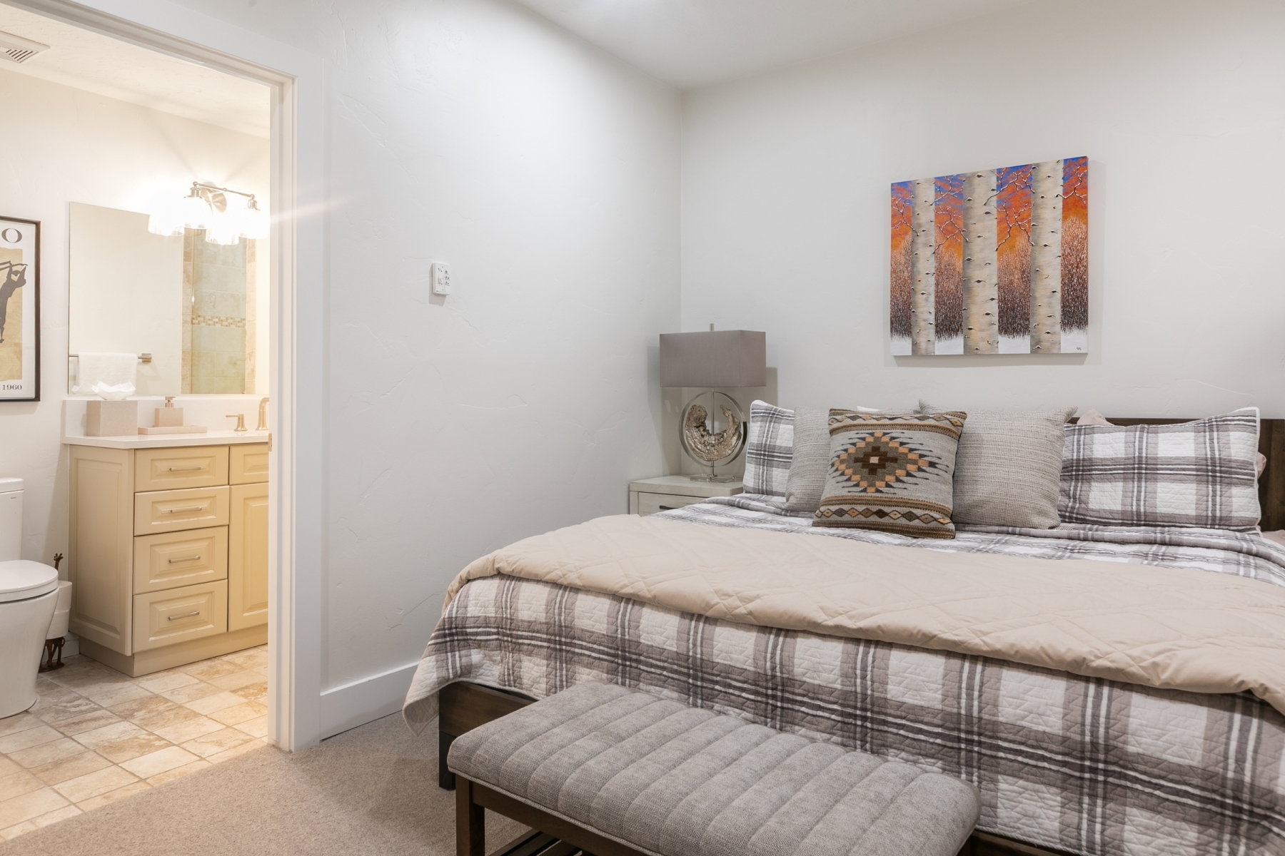 Carpeted bedroom with white walls and an en-suite bathroom featuring a single vanity with light wood cabinetry, a white countertop, and tile flooring
