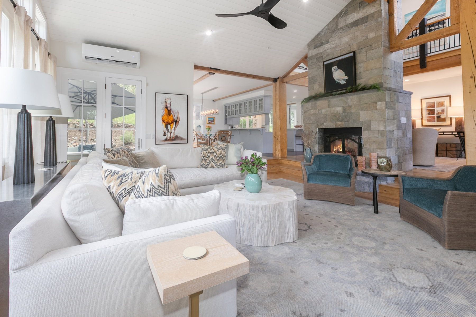 Spacious living area featuring a stone fireplace, vaulted wood-finish ceiling, exposed wood beams, and double French doors opening to the exterior