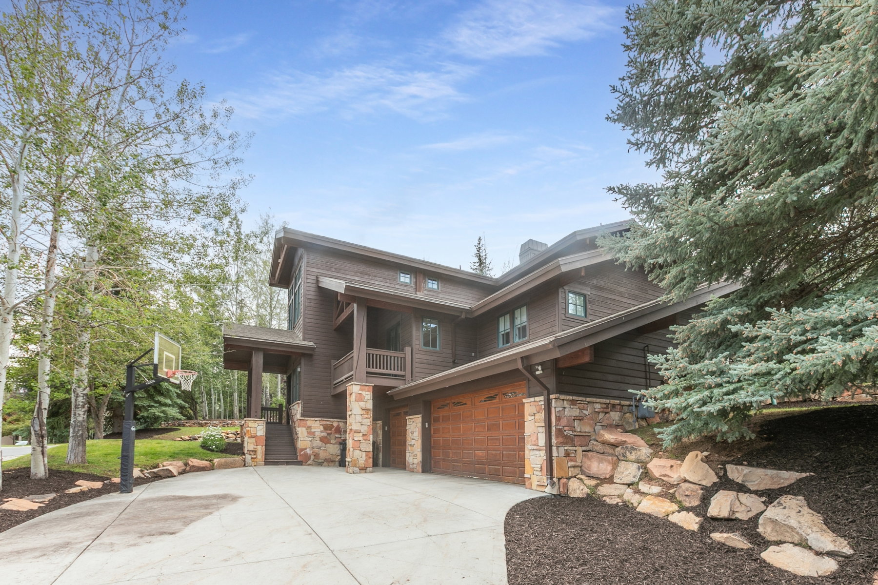 Multi-level exterior with dark wood siding, stone accents, and a two-car garage with wood-finish doors