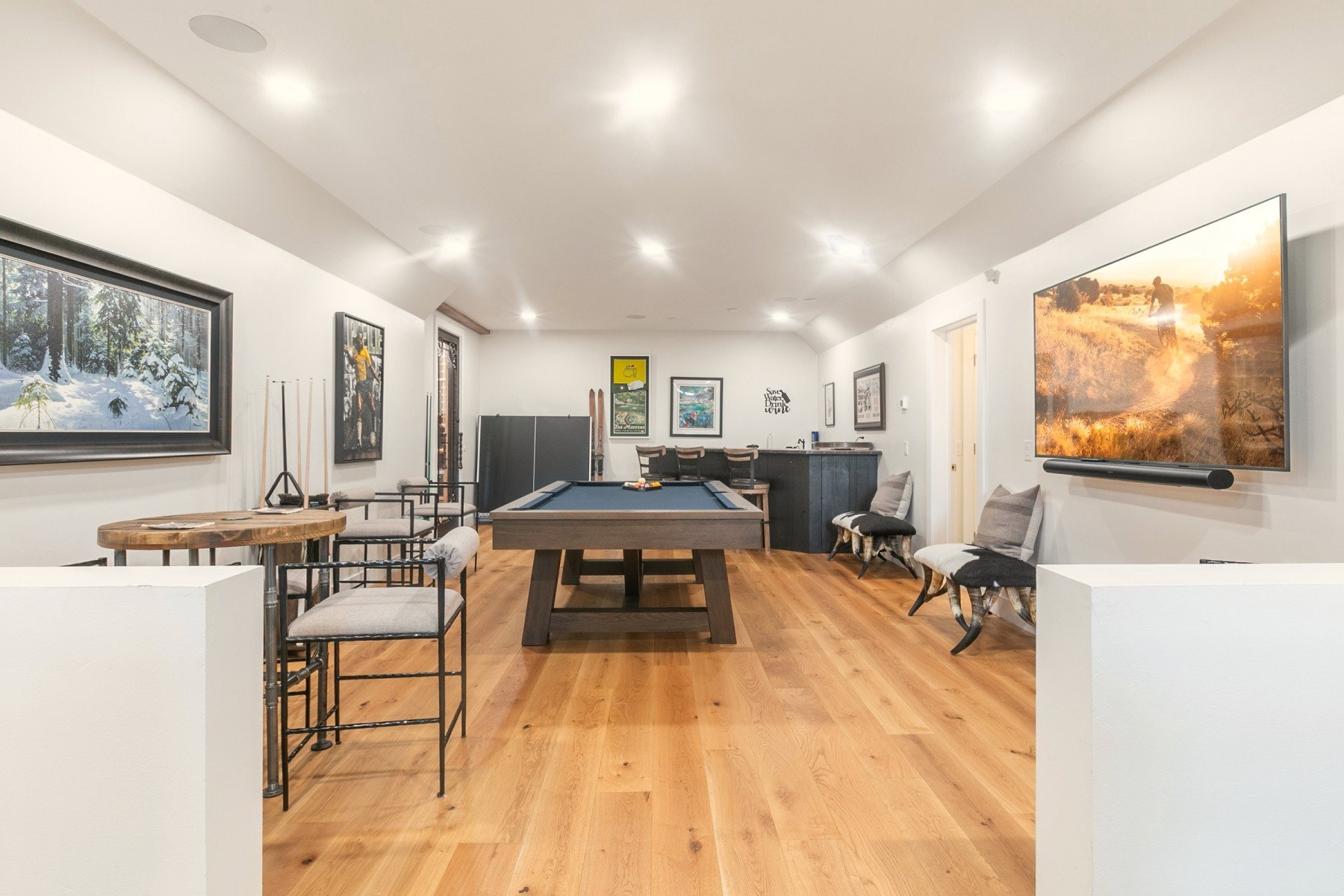Spacious entertainment area featuring wood-finish flooring, recessed lighting, and a mounted flat-screen display