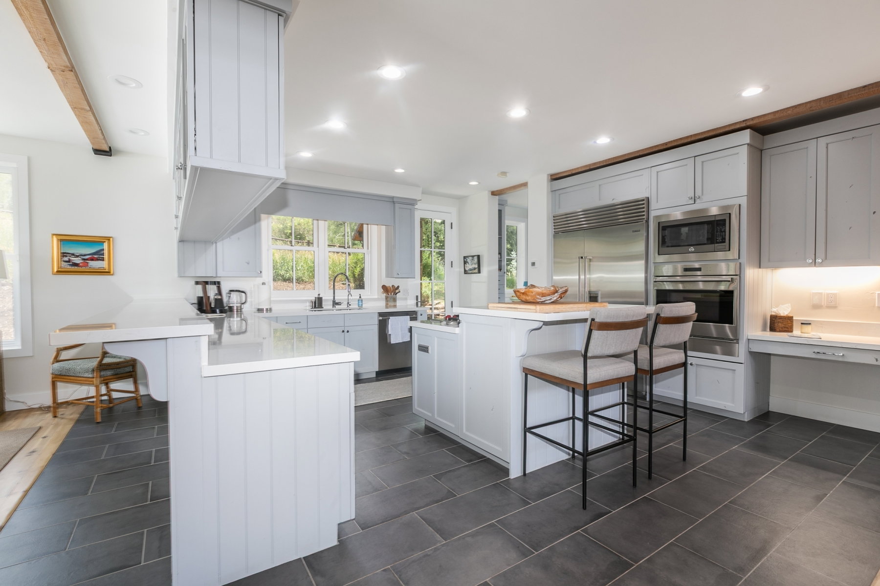 Spacious kitchen featuring large format slate-finish floor tiles, light-toned cabinetry, stainless steel appliances, a center island with a wood-finish countertop, and ample natural light from multiple windows