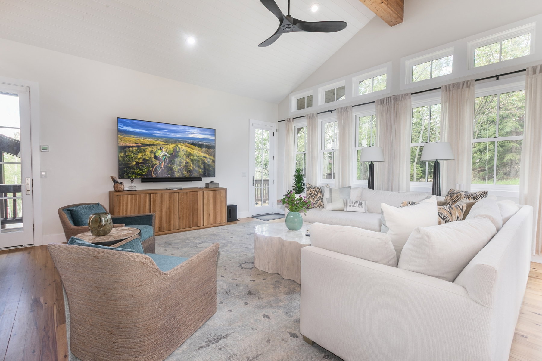 Vaulted ceiling with exposed wood beam, wood-finish flooring, and a wall of windows featuring transom accents