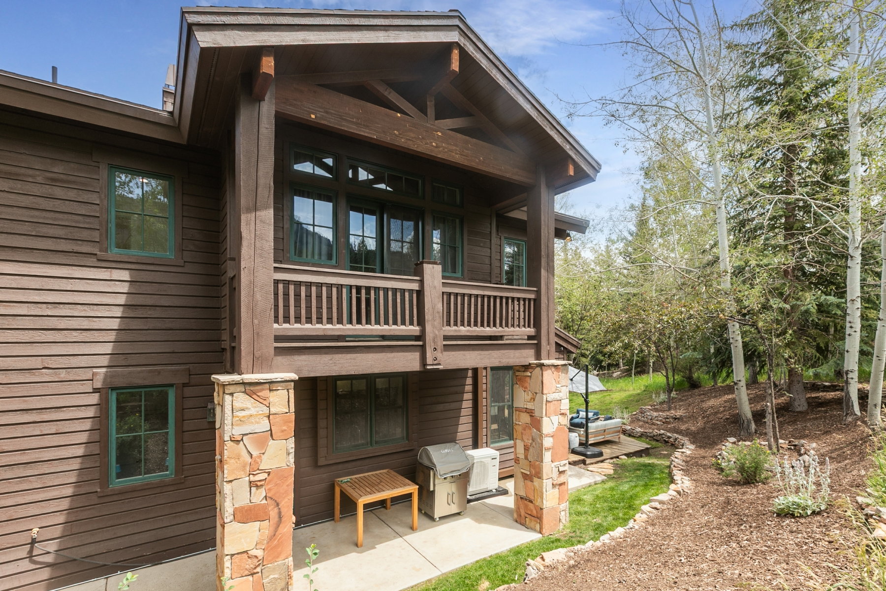 Wood-sided exterior featuring a second-story balcony with wood railing, stone-clad support columns, and green-trimmed windows