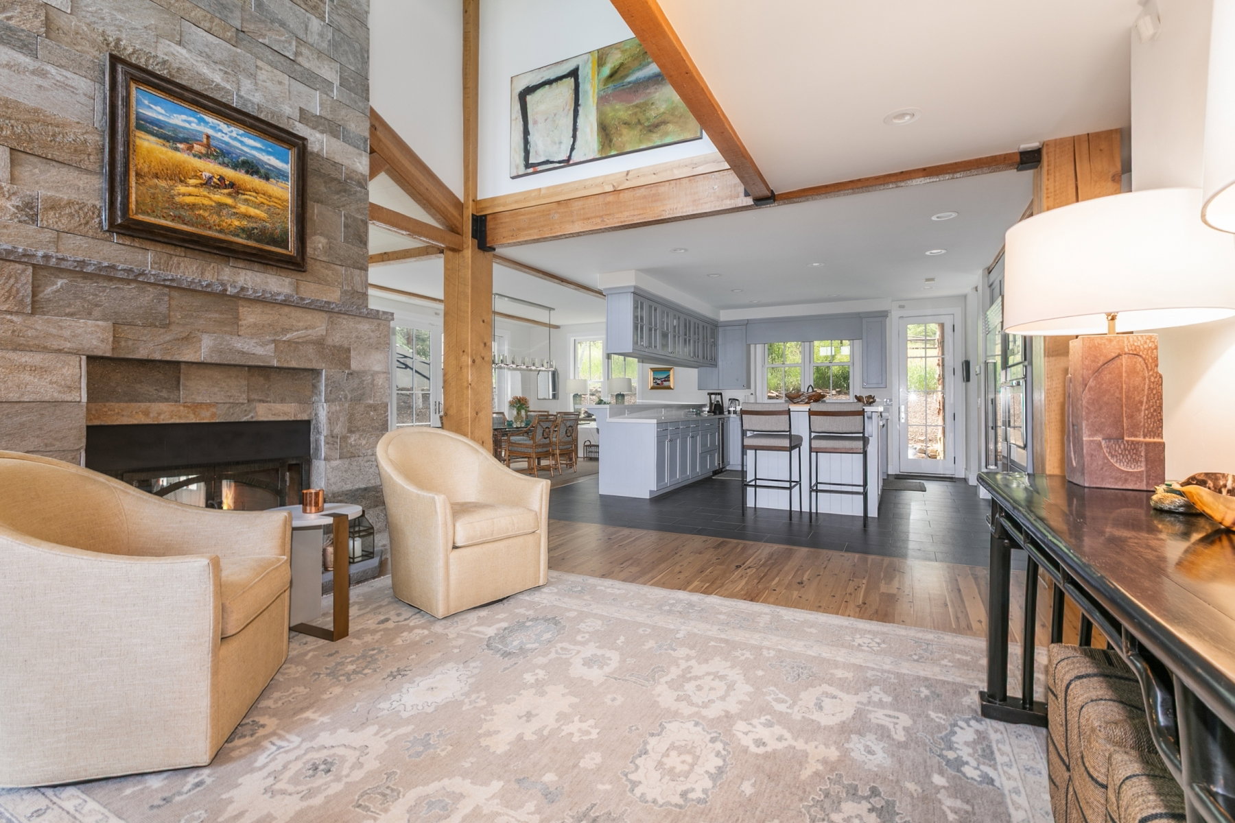 Spacious open-concept living area featuring a floor-to-ceiling stone fireplace, exposed timber beams, and wood-finish flooring