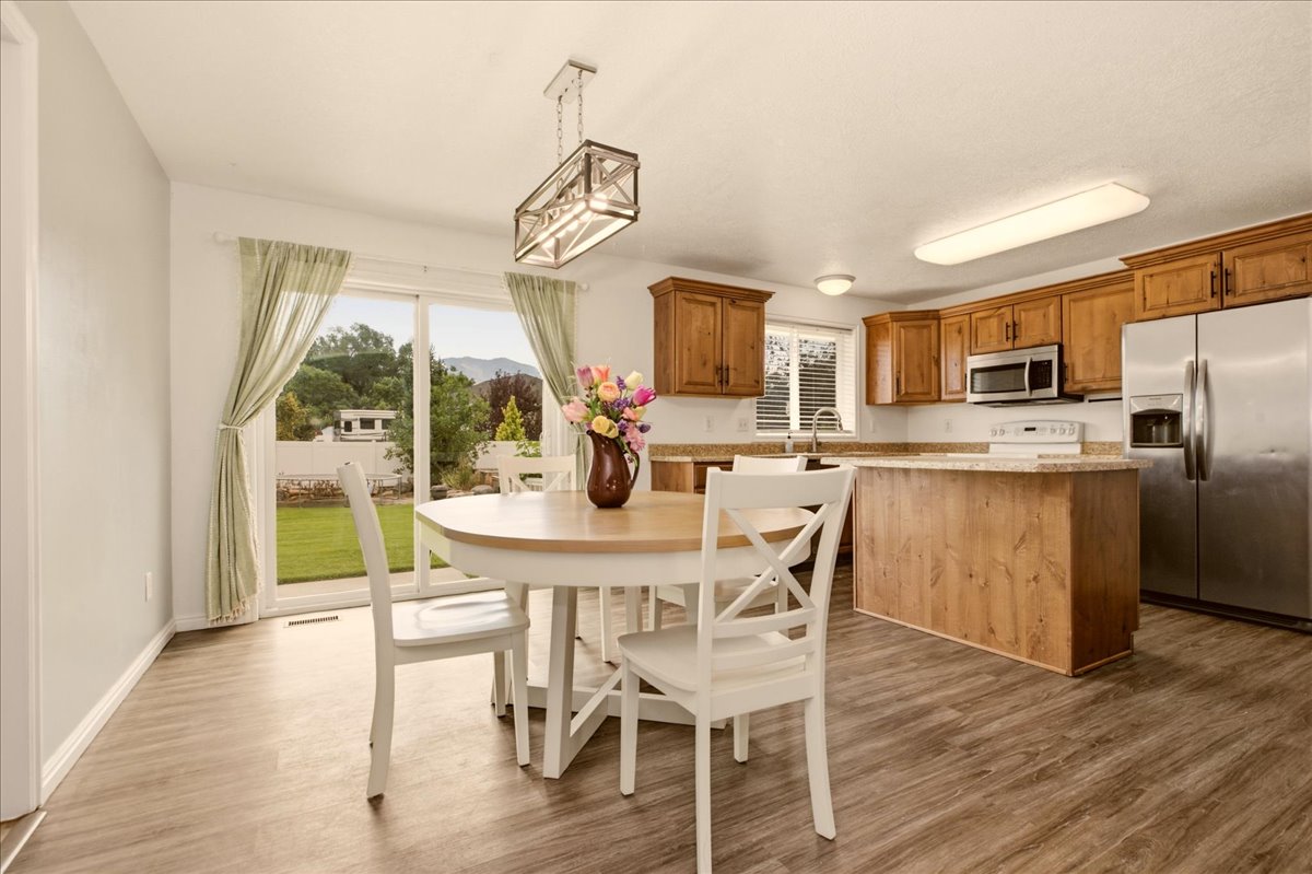 Open-concept kitchen and dining area featuring wood-finish flooring, a kitchen island with seating, natural wood cabinetry, and stainless steel appliances