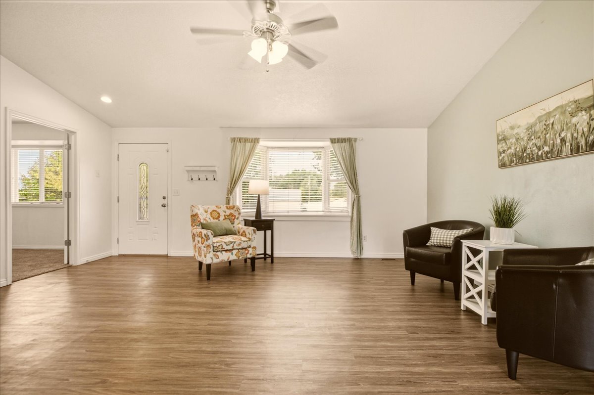 Spacious living area featuring wood-finish flooring, vaulted ceilings, and a ceiling fan with integrated lighting