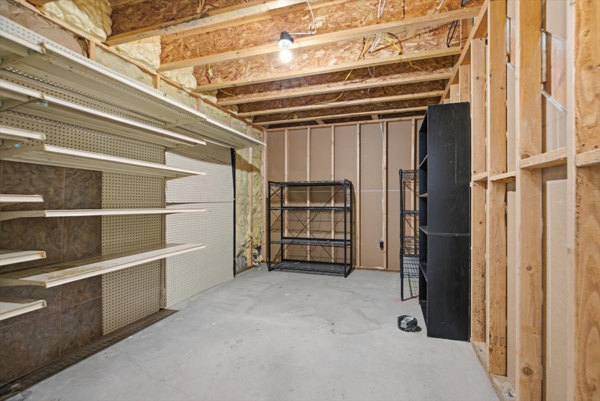 Unfinished basement space featuring exposed wood framing, concrete flooring, and adjustable wall shelving