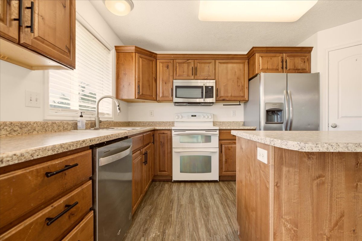 Modern kitchen featuring wood-finish cabinetry, granite-style countertops, and stainless steel appliances including a side-by-side refrigerator, microwave, and dishwasher