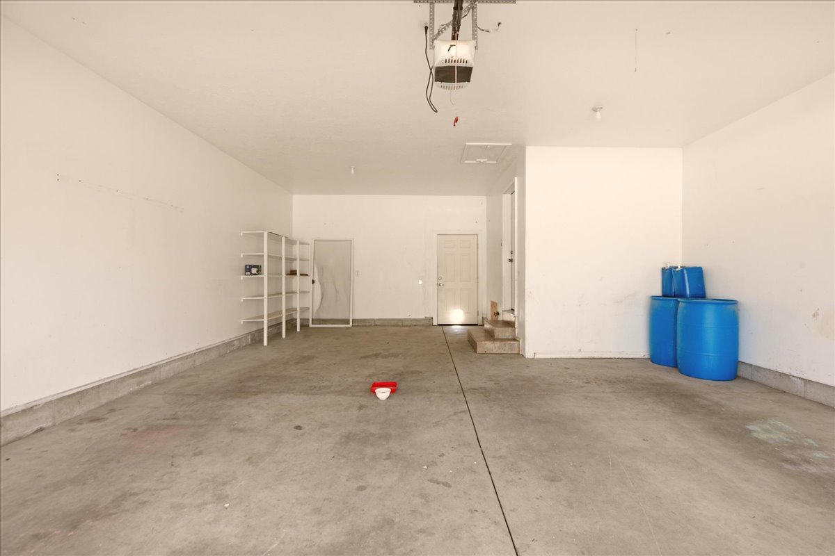 Spacious garage featuring a concrete floor, white painted walls, built-in shelving, and an overhead garage door opener
