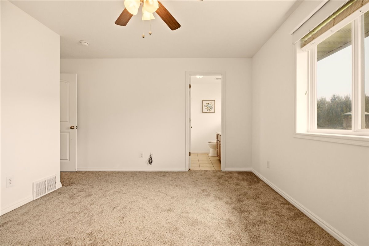 Spacious room featuring neutral carpet, white walls, a ceiling fan with light fixture, and a large window