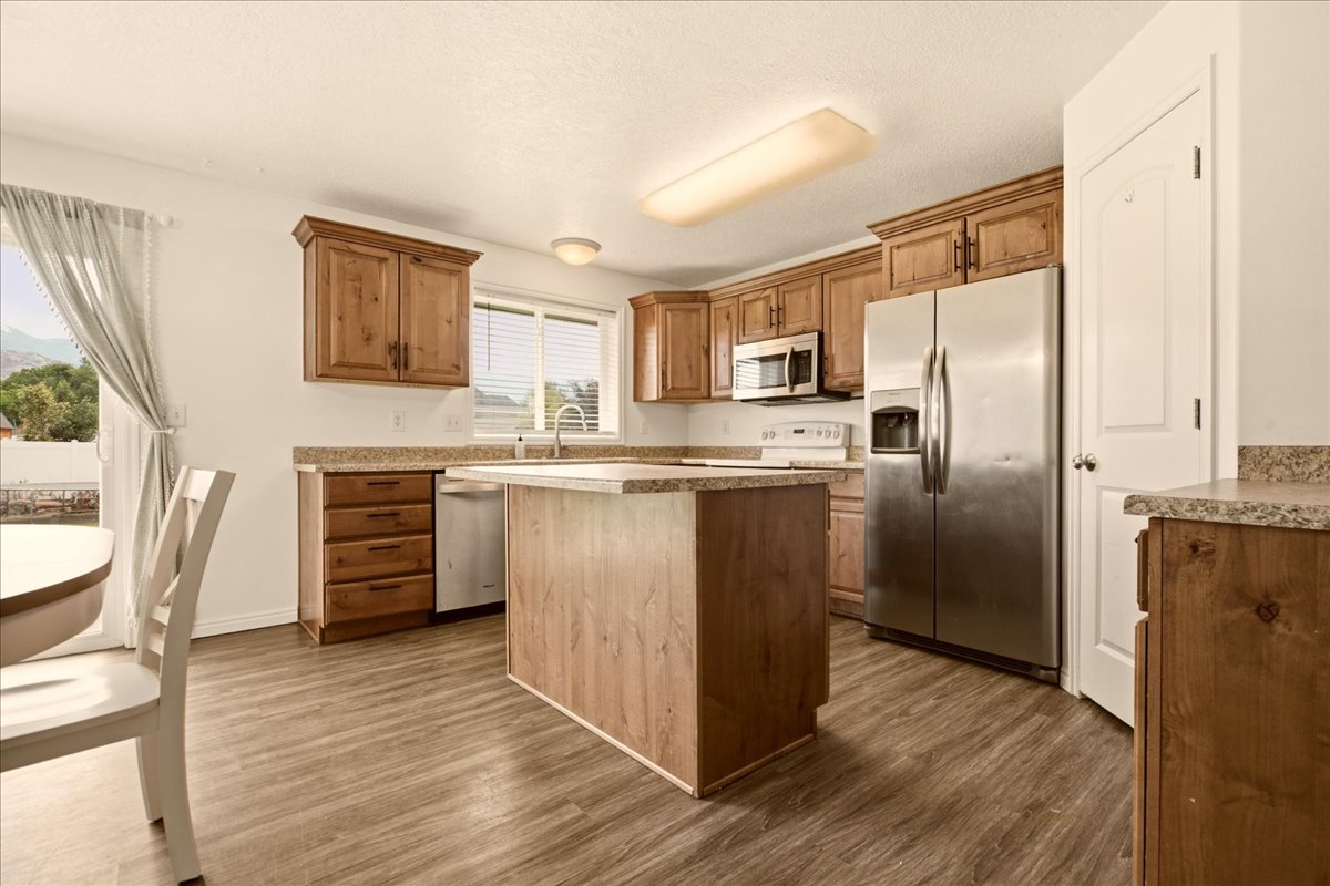 Kitchen featuring wood-finish flooring, wood cabinetry, stone-look countertops, a central island, and stainless steel appliances