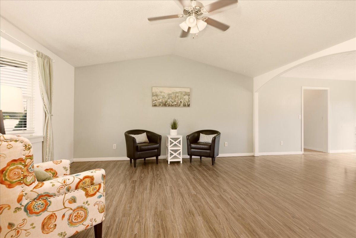 Spacious interior with vaulted ceilings, wood-finish flooring, a ceiling fan, and an arched entryway