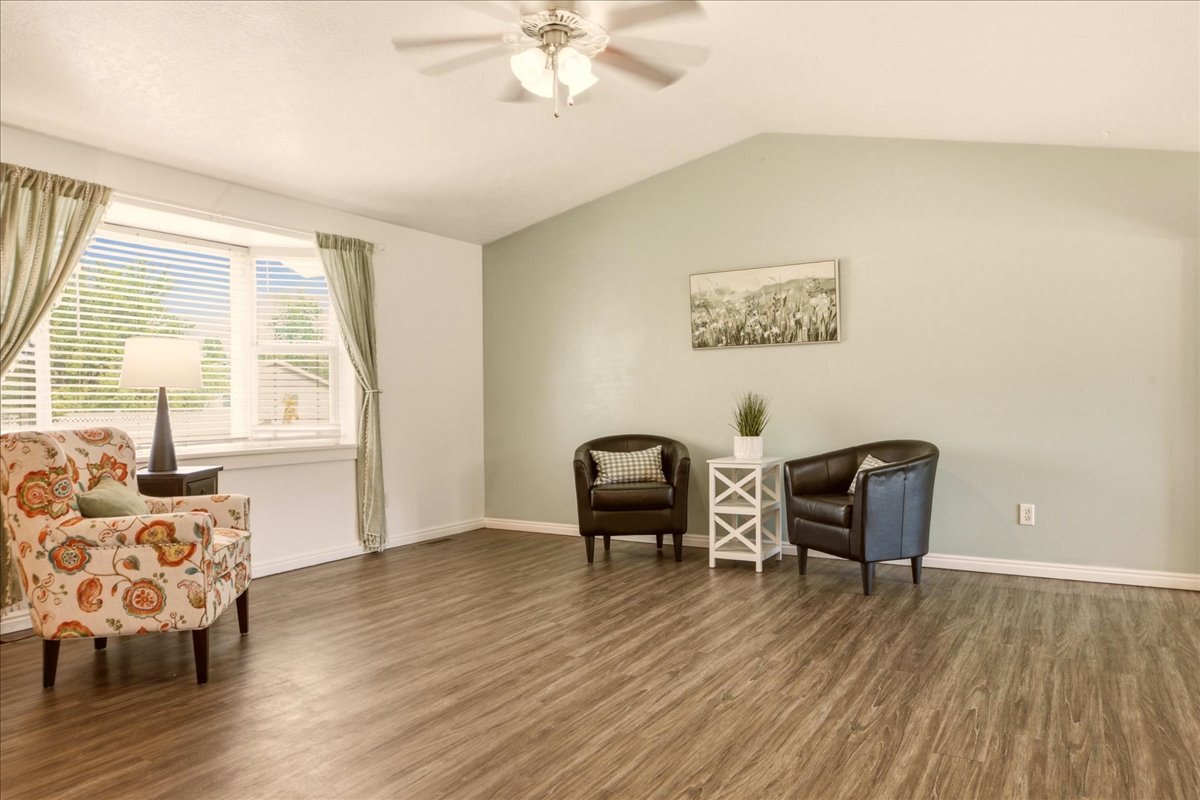 Spacious living area featuring wood-finish flooring, a vaulted ceiling, and a ceiling fan