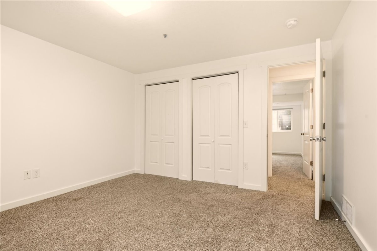 Carpeted room featuring white walls, baseboards, and two bi-fold closet doors with panel detailing