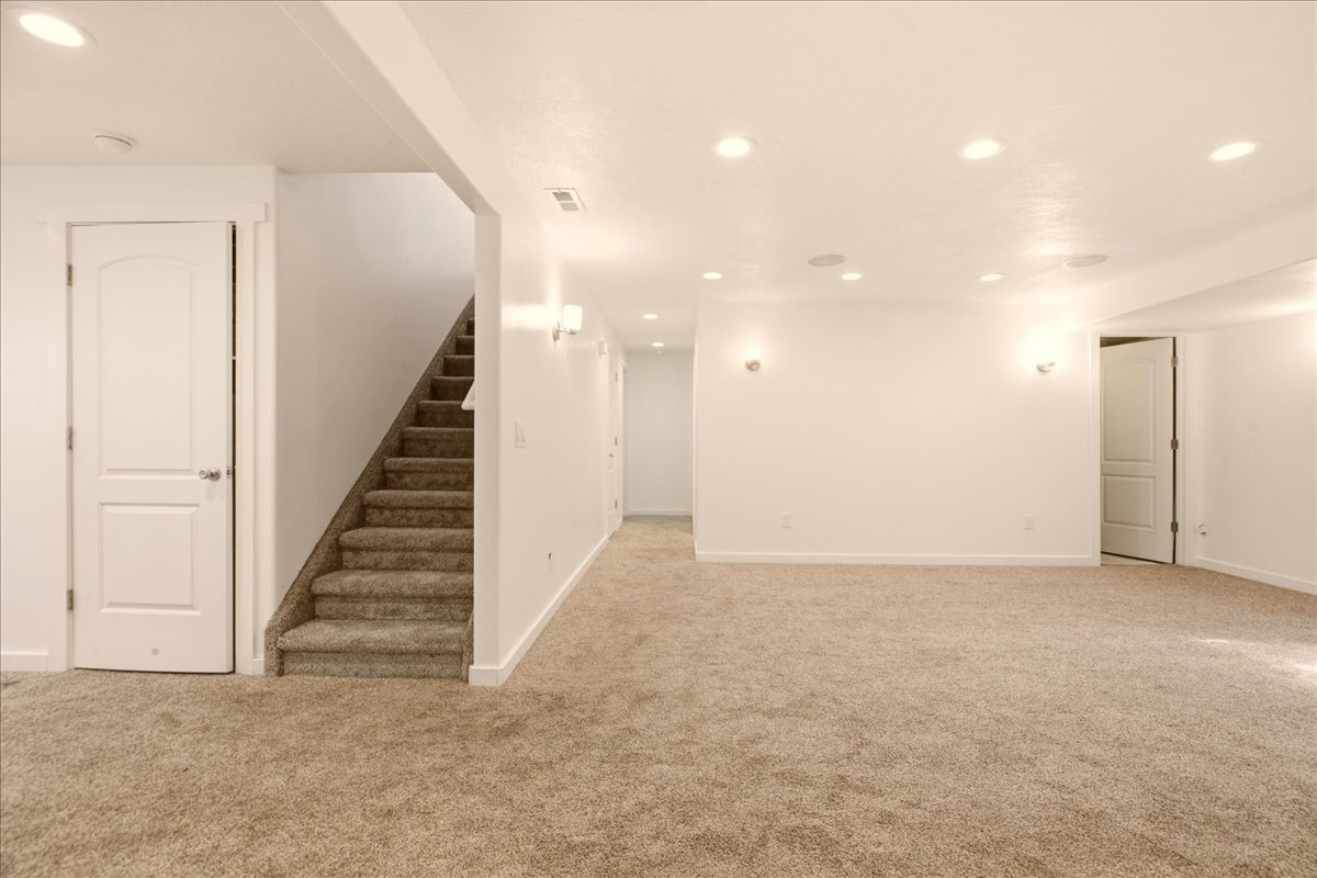 Spacious carpeted room featuring recessed lighting, wall sconces, a two-panel interior door, and a carpeted staircase