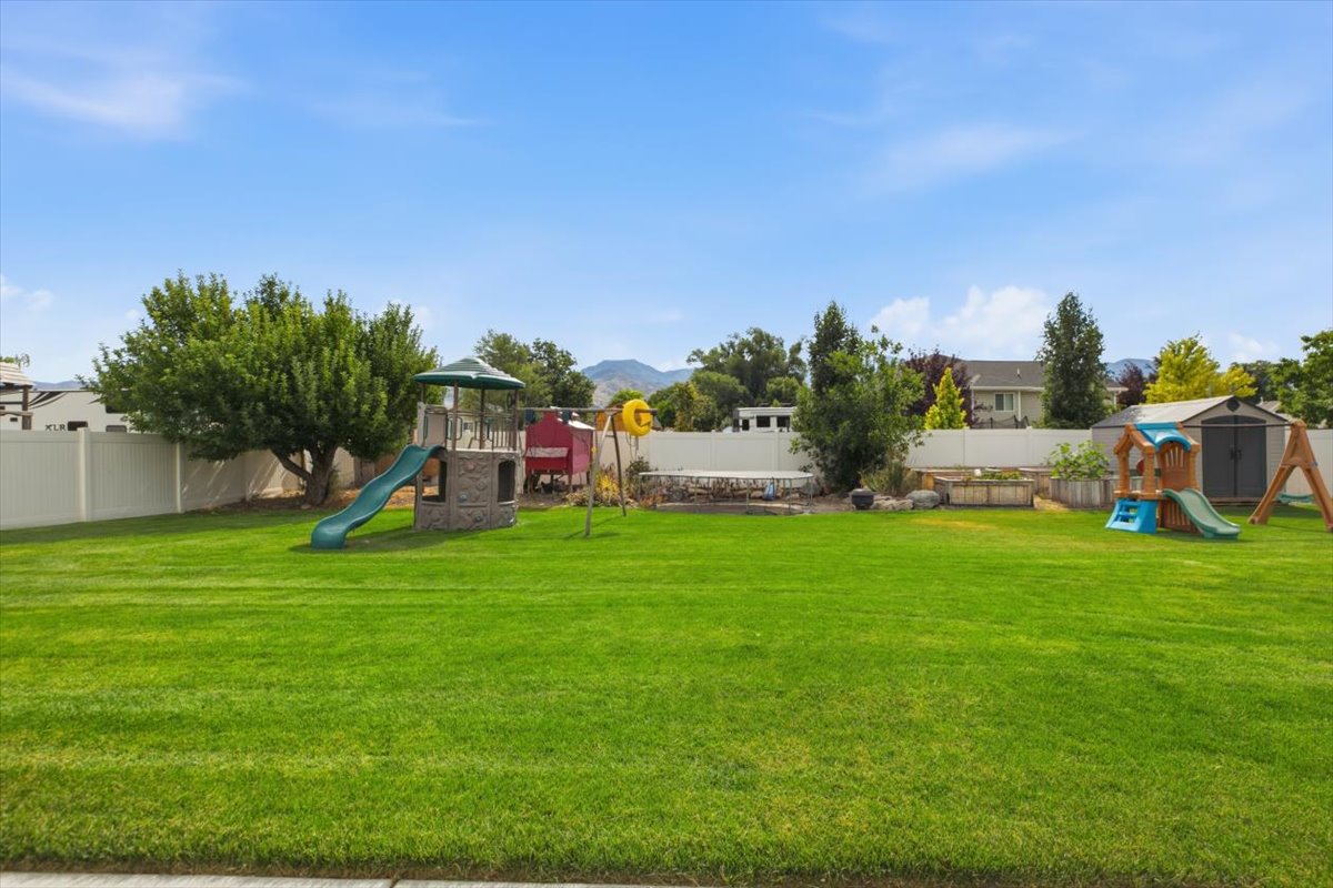 Expansive backyard featuring a lush lawn, white privacy fencing, mature trees, and a visible mountain backdrop