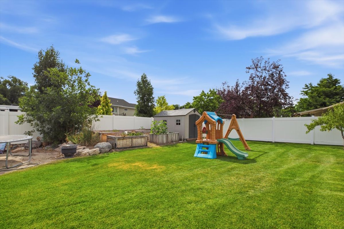 Expansive backyard featuring a manicured lawn, white privacy fencing, raised garden beds, and a storage shed