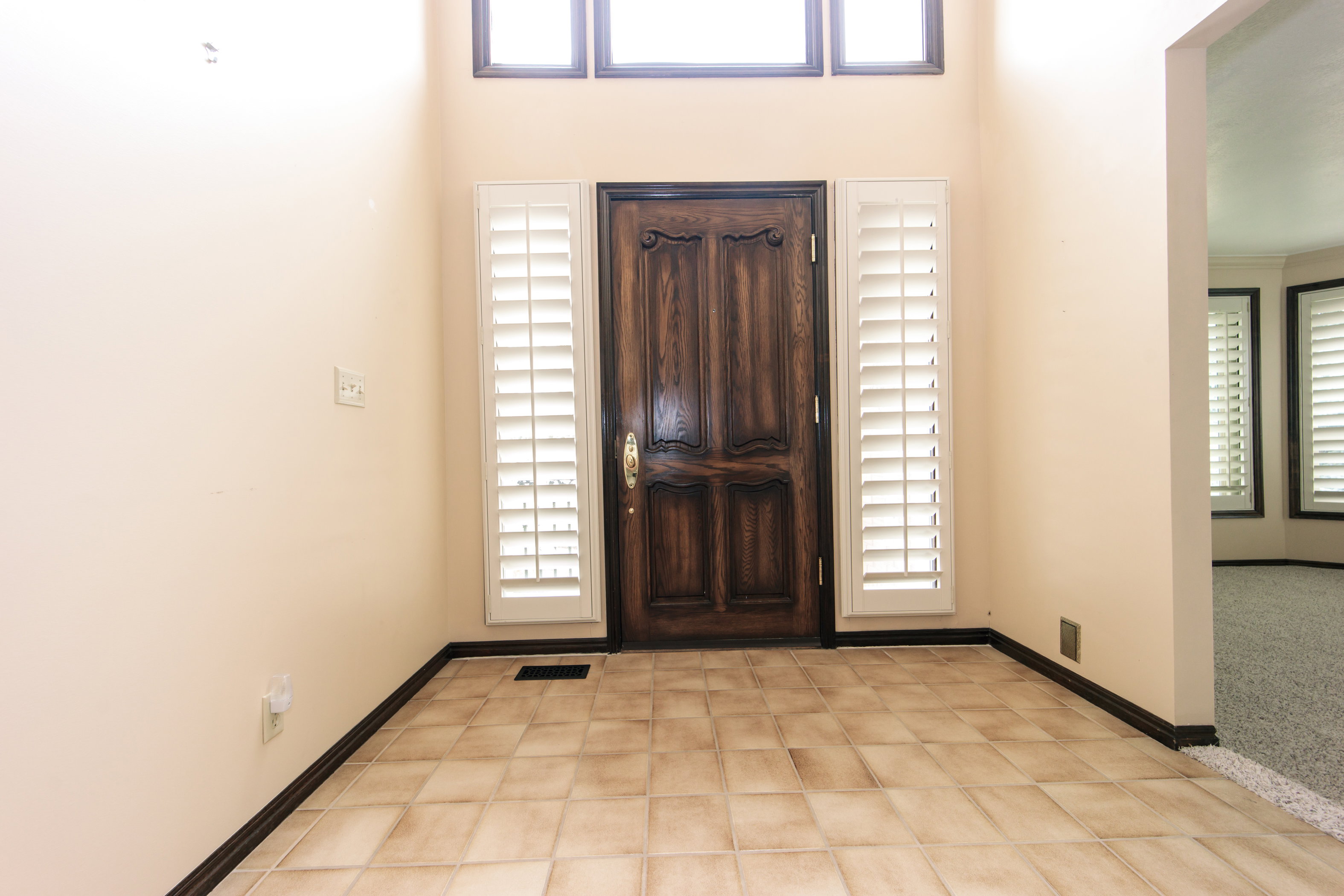 Entryway featuring a carved wooden front door with sidelights, tile flooring, and overhead transom windows